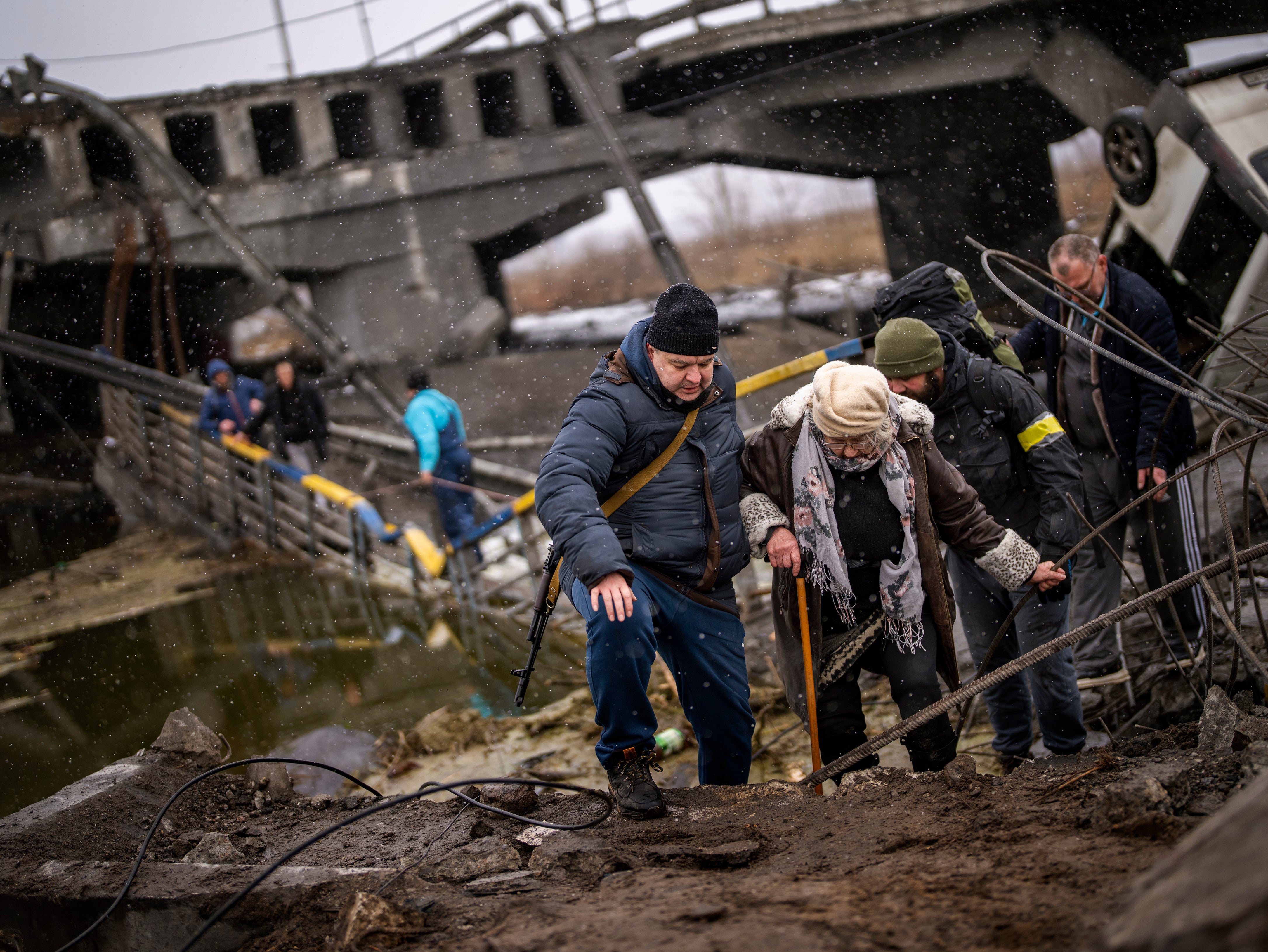 Local militiamen help an old woman crossing a bridge destroyed by artillery