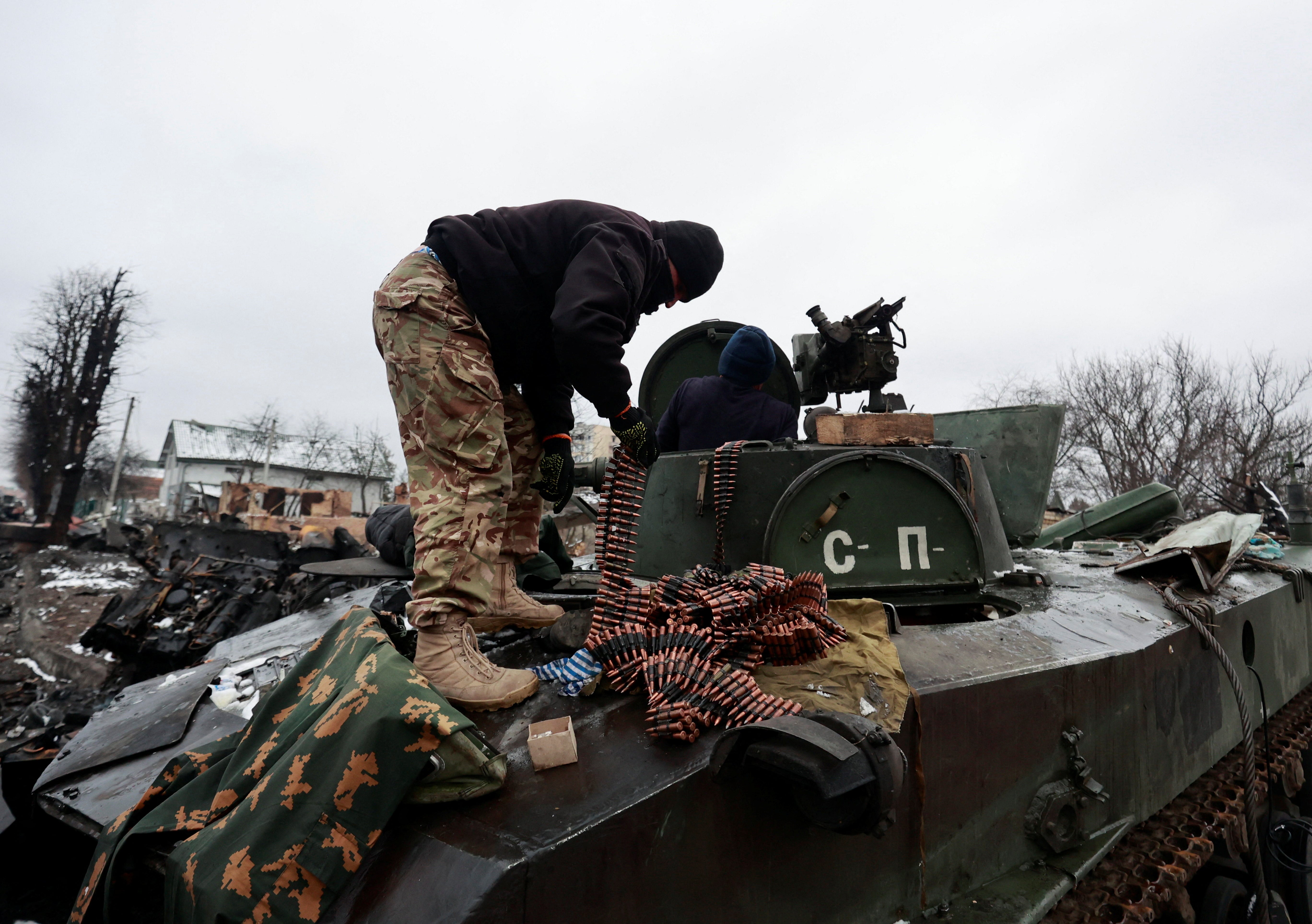 Local residents pick up ammunition from a destroyed armoured vehicle, in the town of Bucha, Kyiv region