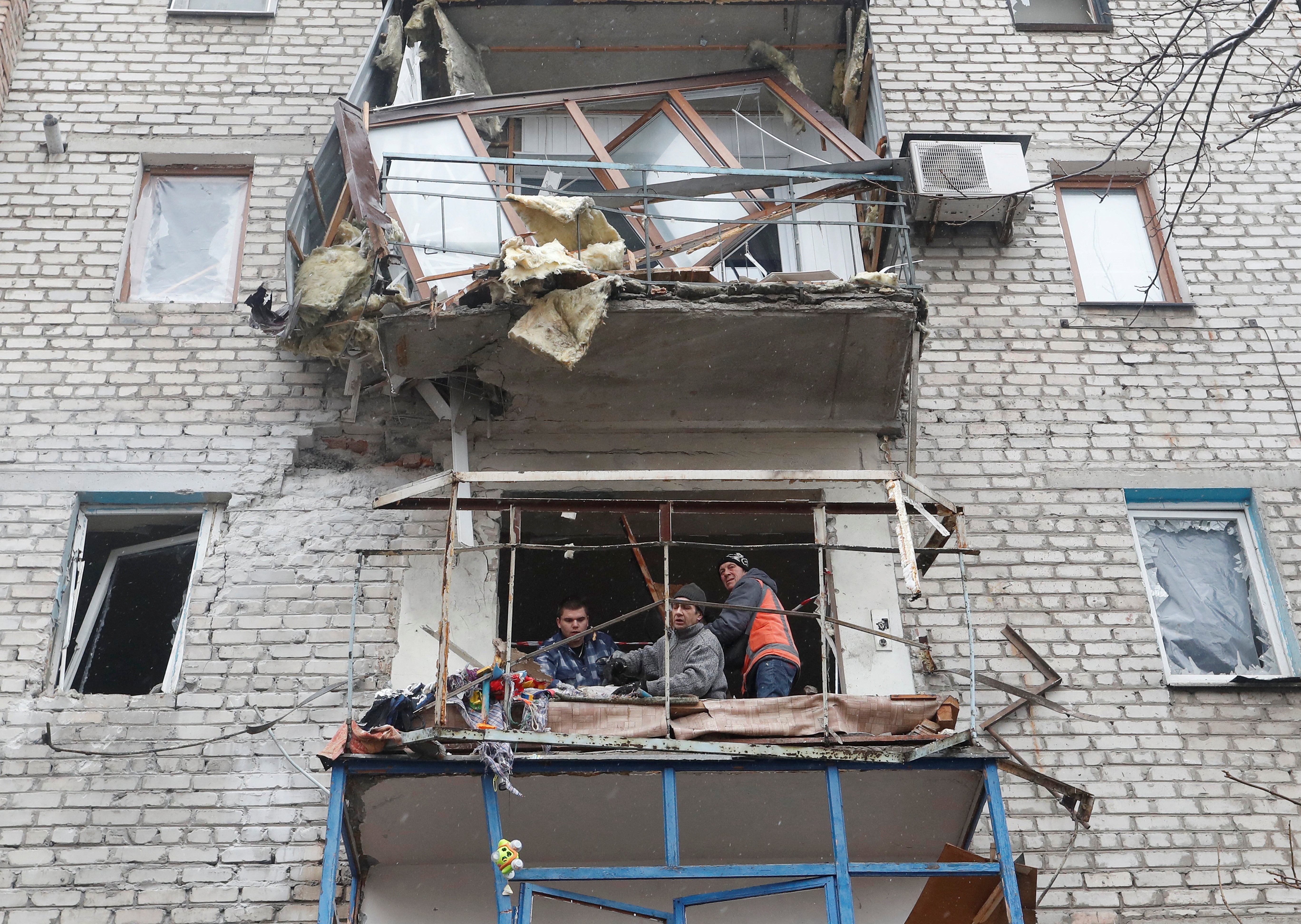 People remove debris from an apartment building in the town of Yasynuvata
