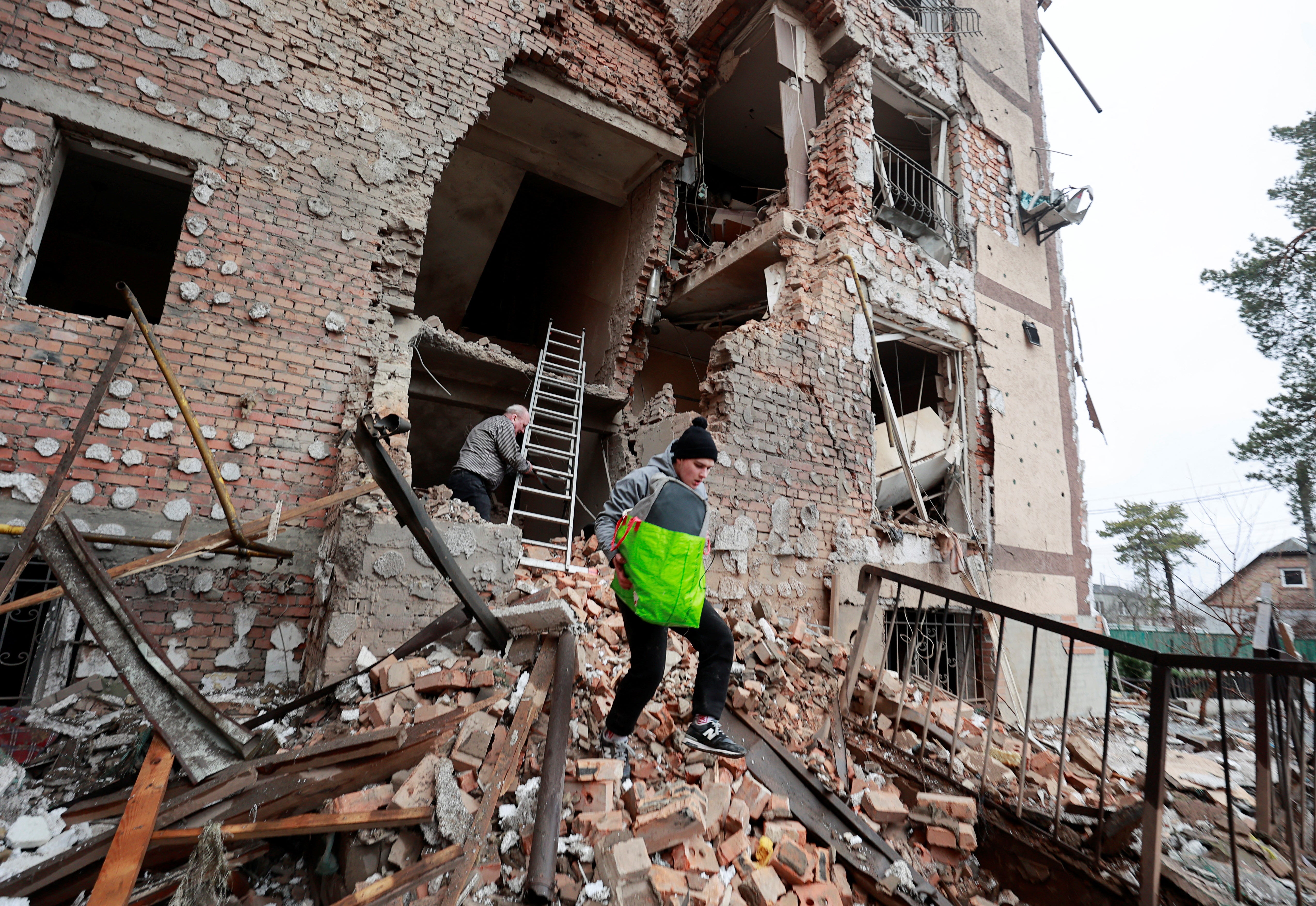 People carry belongings out of a residential building destroyed by recent shelling in the city of Irpin