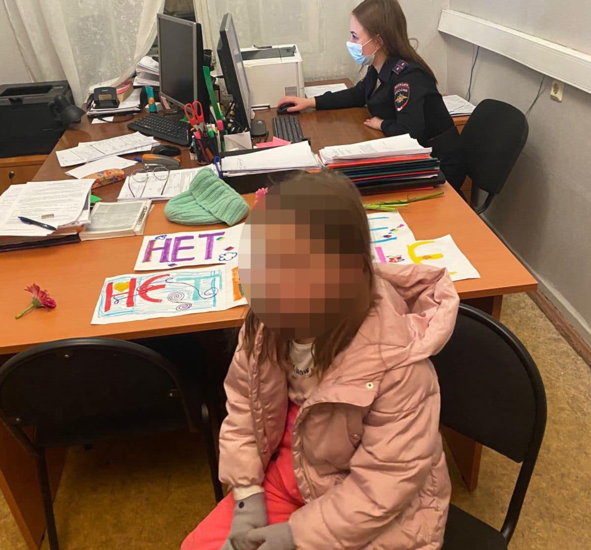 Homemade anti-war banners can be seen lying on a desk beside one of the detained children as a woman in police uniform works on a computer in the background