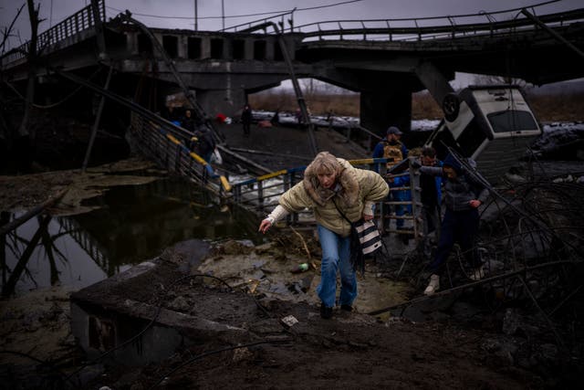 A woman runs as she flees with her family across a destroyed bridge in the outskirts of Kyiv (Emilio Morenatti/AP/PA)