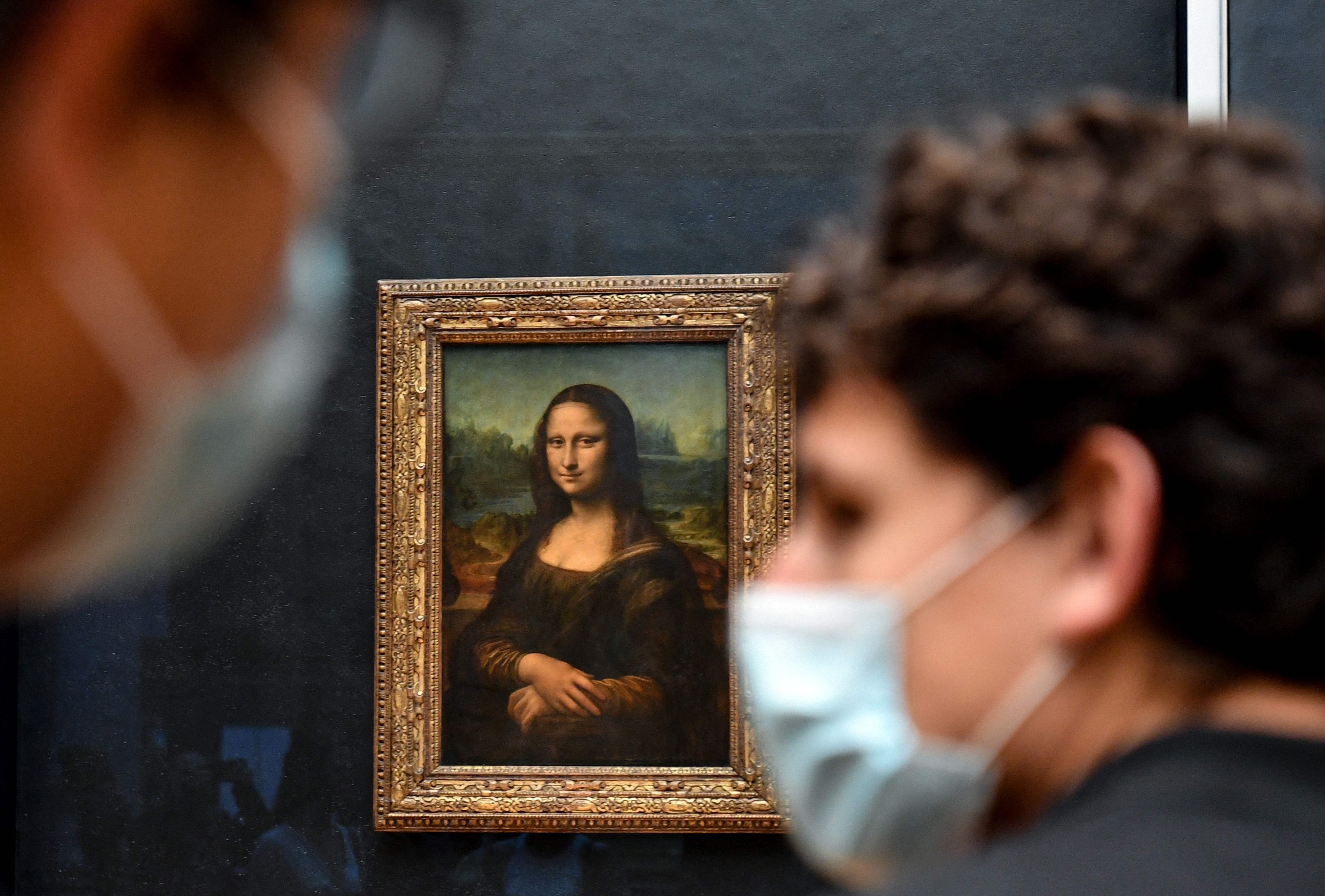 In this photo taken on May 19, 2021 visitors walk past the painting "La Joconde" The Mona Lisa by Italian artist Leonardo Da Vinci on display in the "Salle des Etats" at The Louvre Museum in Paris