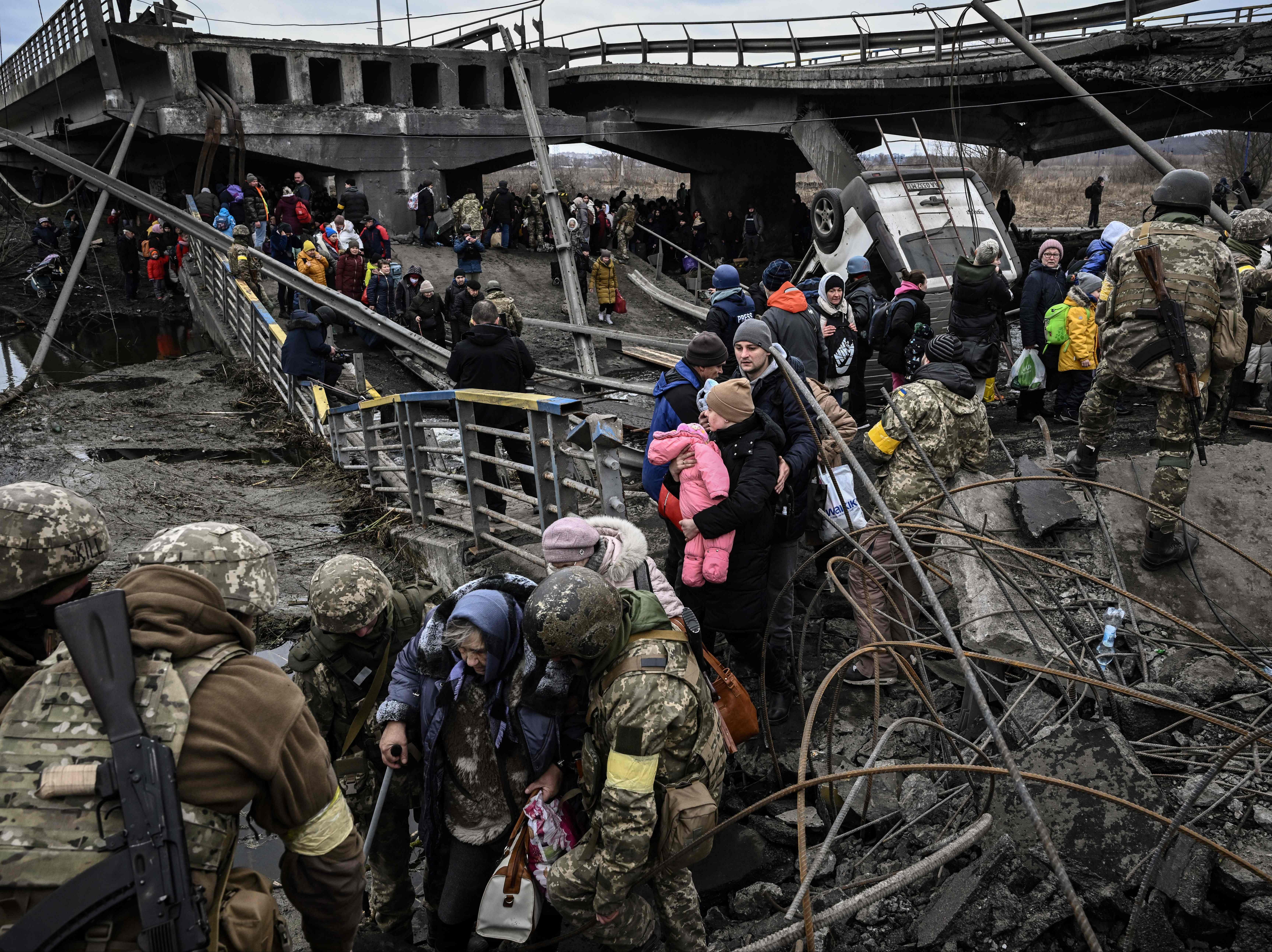 People cross a destroyed bridge as they evacuate the city of Irpin, northwest of Kyiv, during heavy shelling