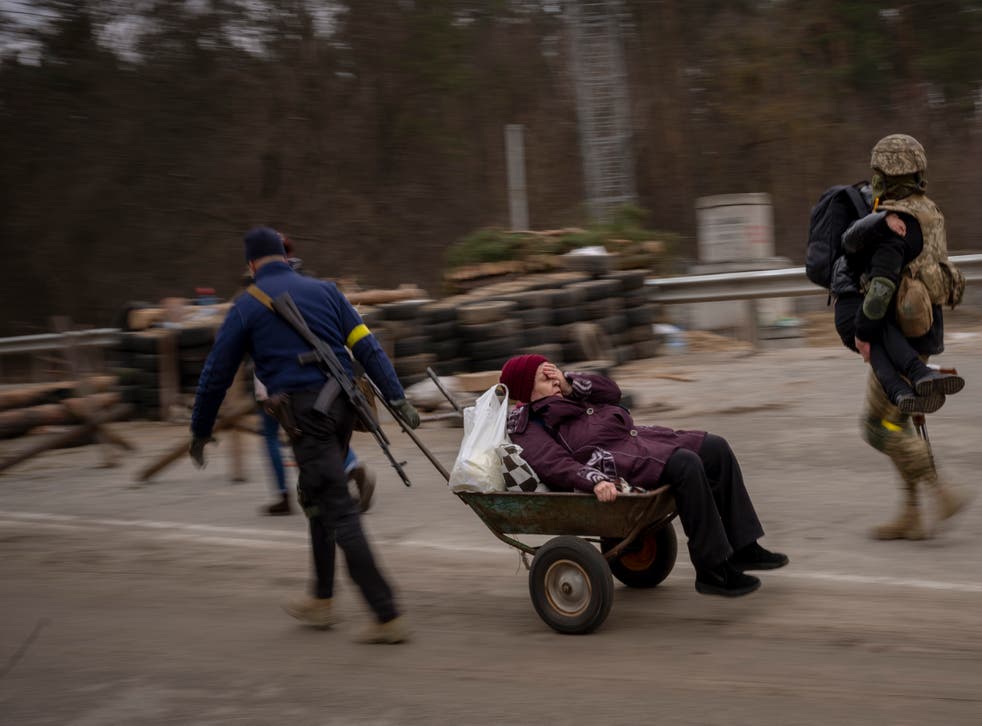 A Ukrainian soldier and a militia man help a fleeing family crossing the Irpin River on the outskirts of Kyiv, Ukraine (Emilio Morenatti/AP)