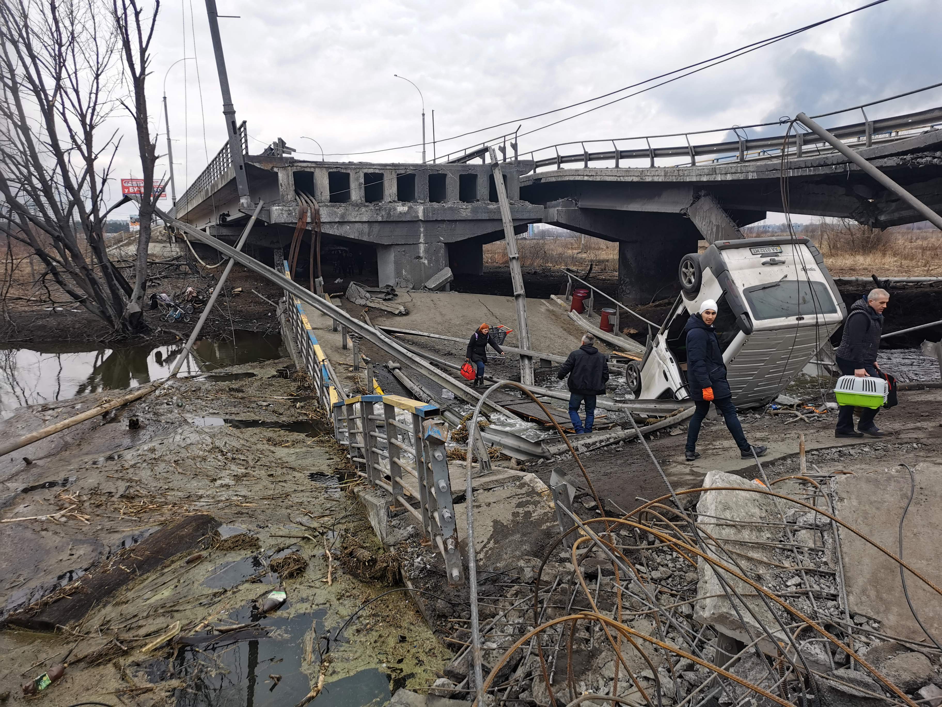 Pedestrians cross a destroyed bridge as they evacuate the city of Irpin, northwest of Kyiv, 6 March 2022