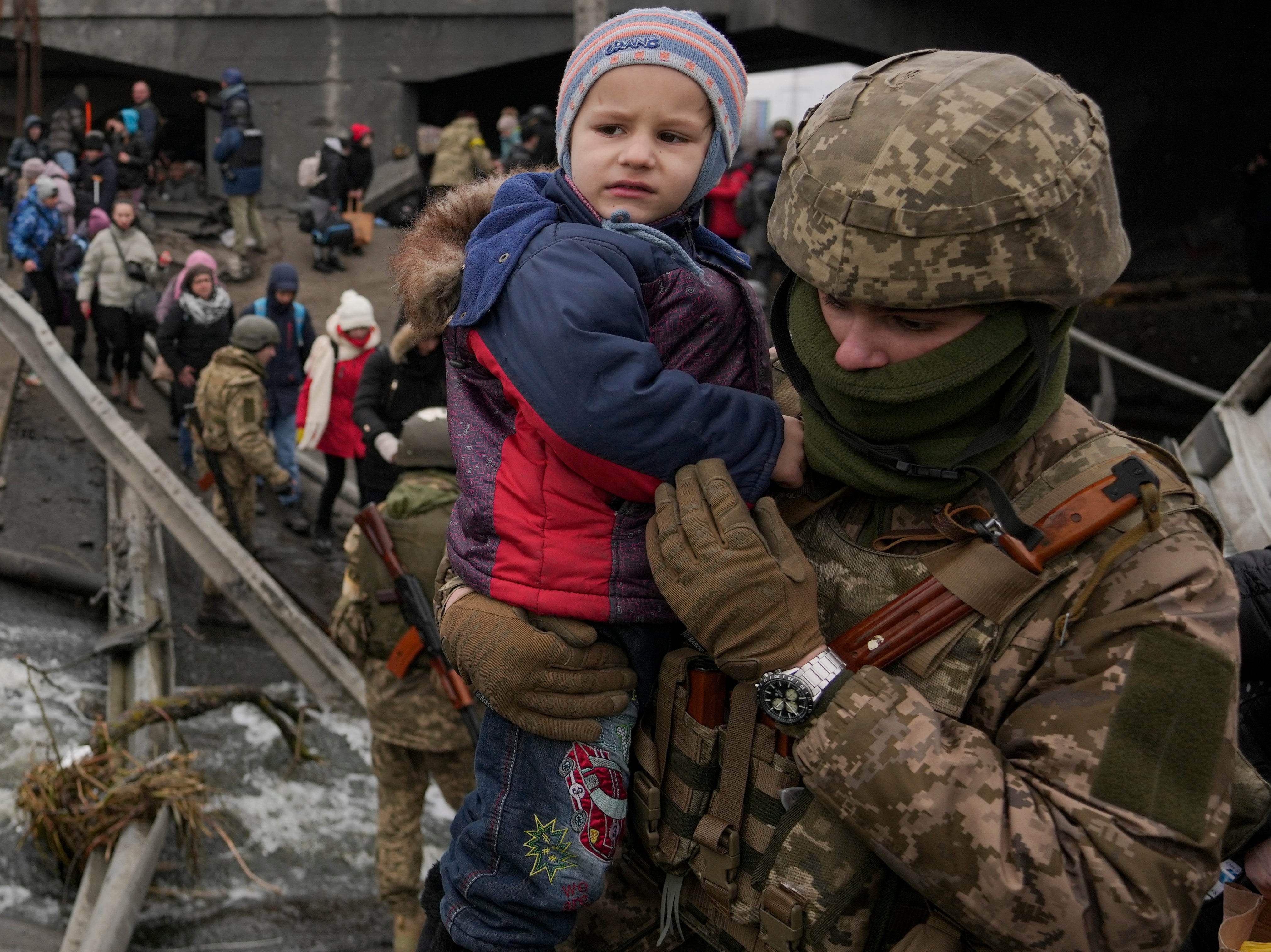 A Ukrainian soldier holds a child crossing the River Irpin