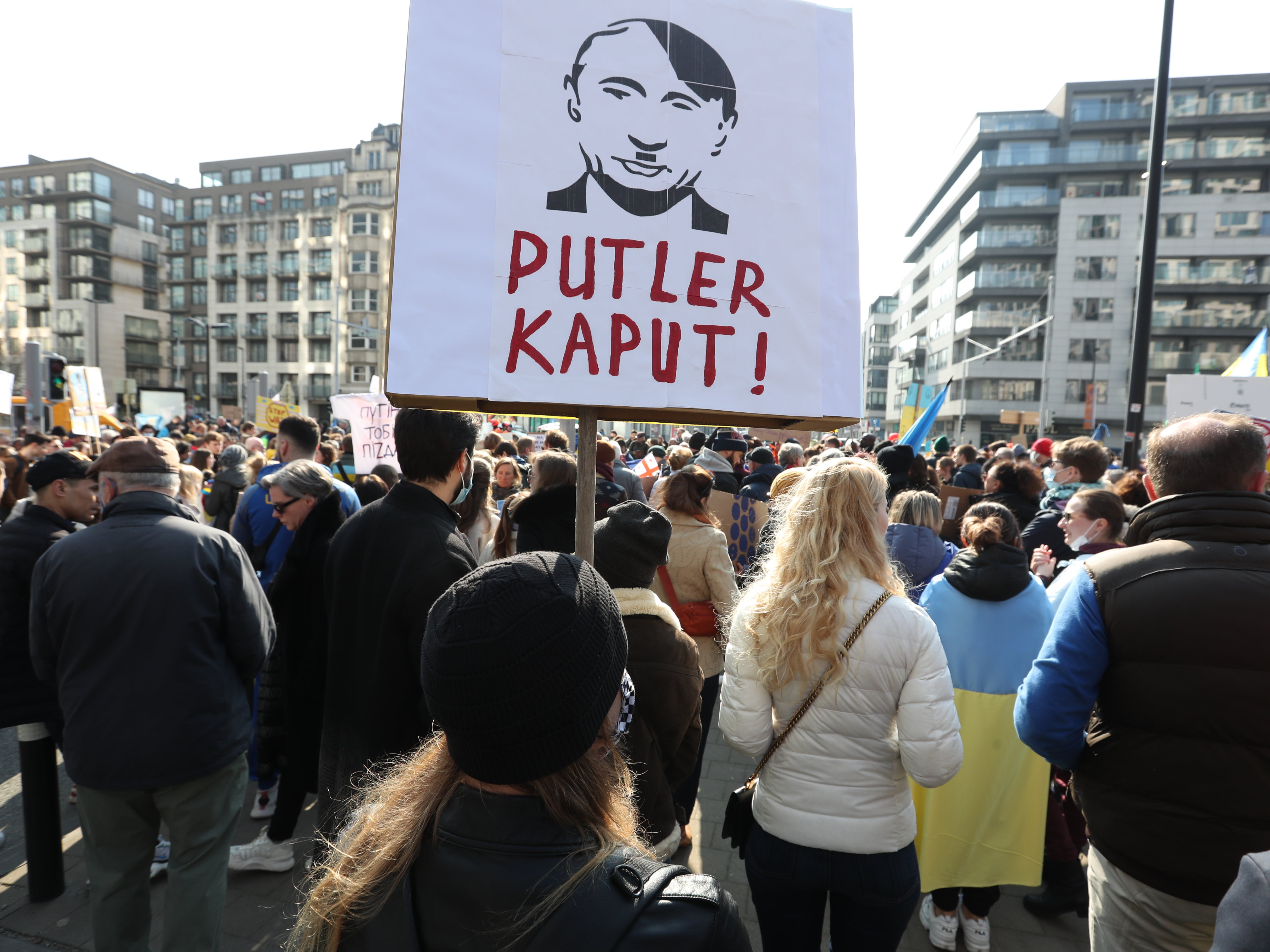 <p>A protester in Brussels carries a sign that shows a mash-up portrait of Putin and Hitler</p>