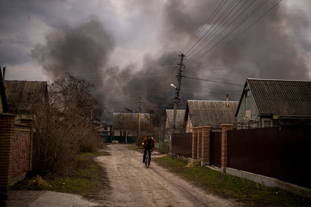 <p>A Ukrainian man rides his bicycle near to a factory and a store burning after been bombarded in Irpin</p>