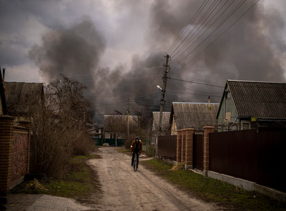A Ukrainian man rides his bicycle near a factory and a store burning after it had been bombarded in Irpin, on the outskirts of Kyiv (AP)