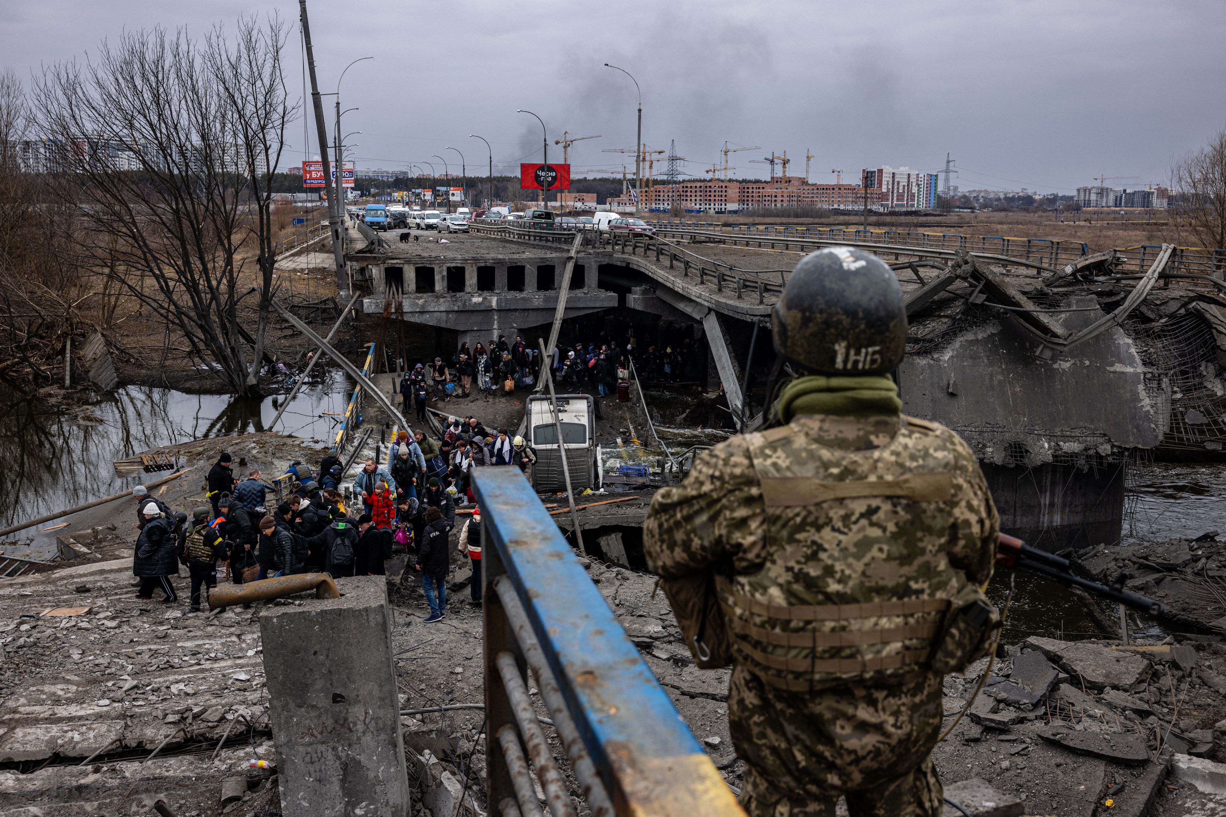 A Ukrainian serviceman looks on as evacuees cross a destroyed bridge as they flee the city of Irpin, northwest of Kyiv, on 7 March 2022