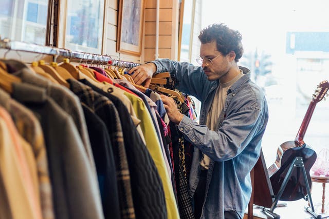 <p>A man looking through second hand clothes at a charity shop in Newcastle-upon-Tyne. According to academics people should limit themselves to buying three new items of clothing a year</p>