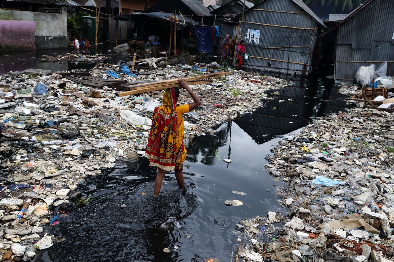 A woman carries firewood on her head while passing through water on her way to home during a monsoon in Dhaka, Bangladesh