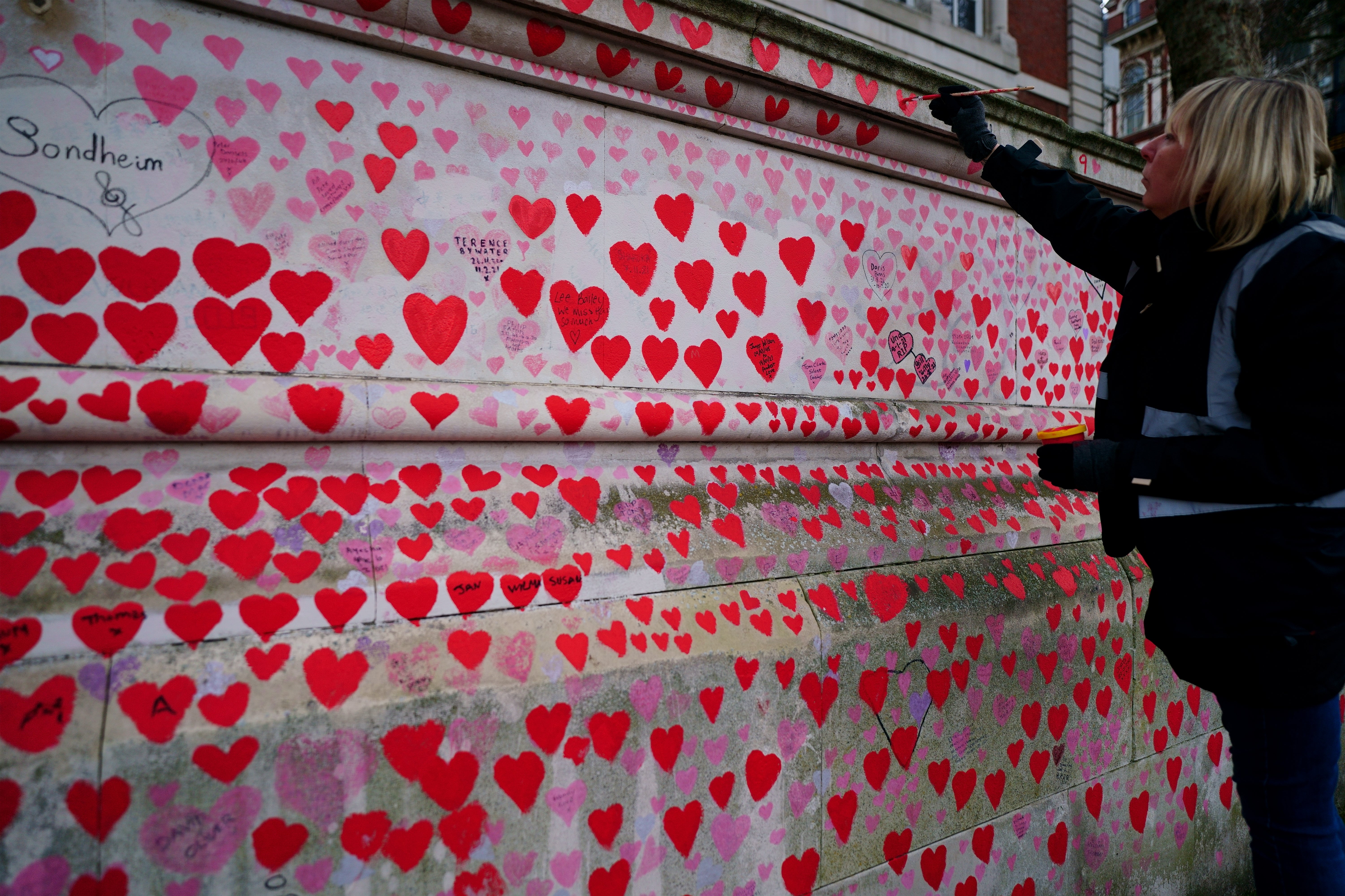 A volunteer from the Covid-19 Bereaved Families for Justice campaign group paints a heart on the Covid memorial wall in Westminster, central London (Victoria Jones/PA)
