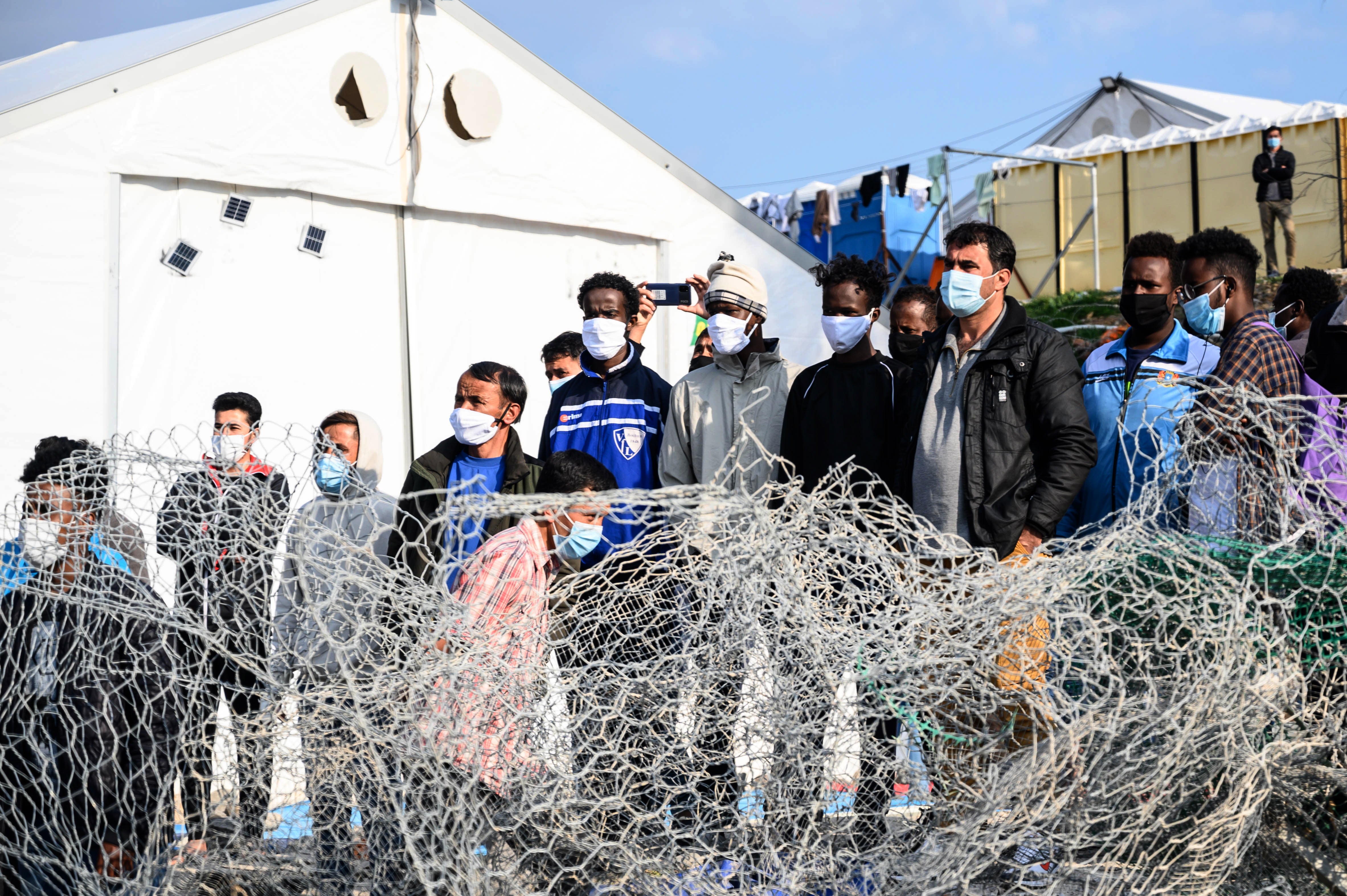 File photo: Migrants stand behind a fence at Karatepe refugee camp on Lesbos island, Greece, 29 March 2021