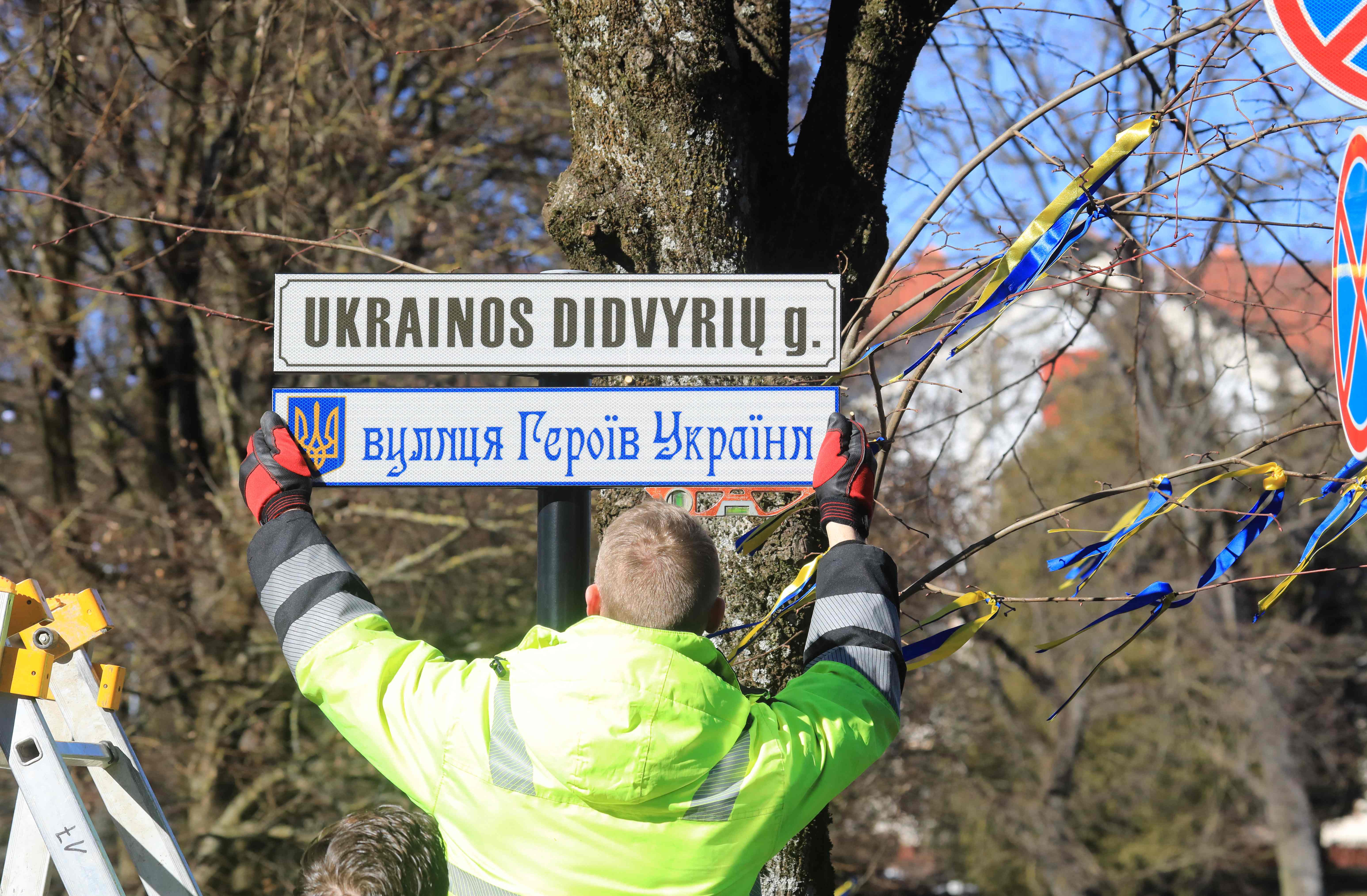 A worker fixes street plates in Lithuanian and in Ukrainian languages reading "Ukrainian Heroes Street"