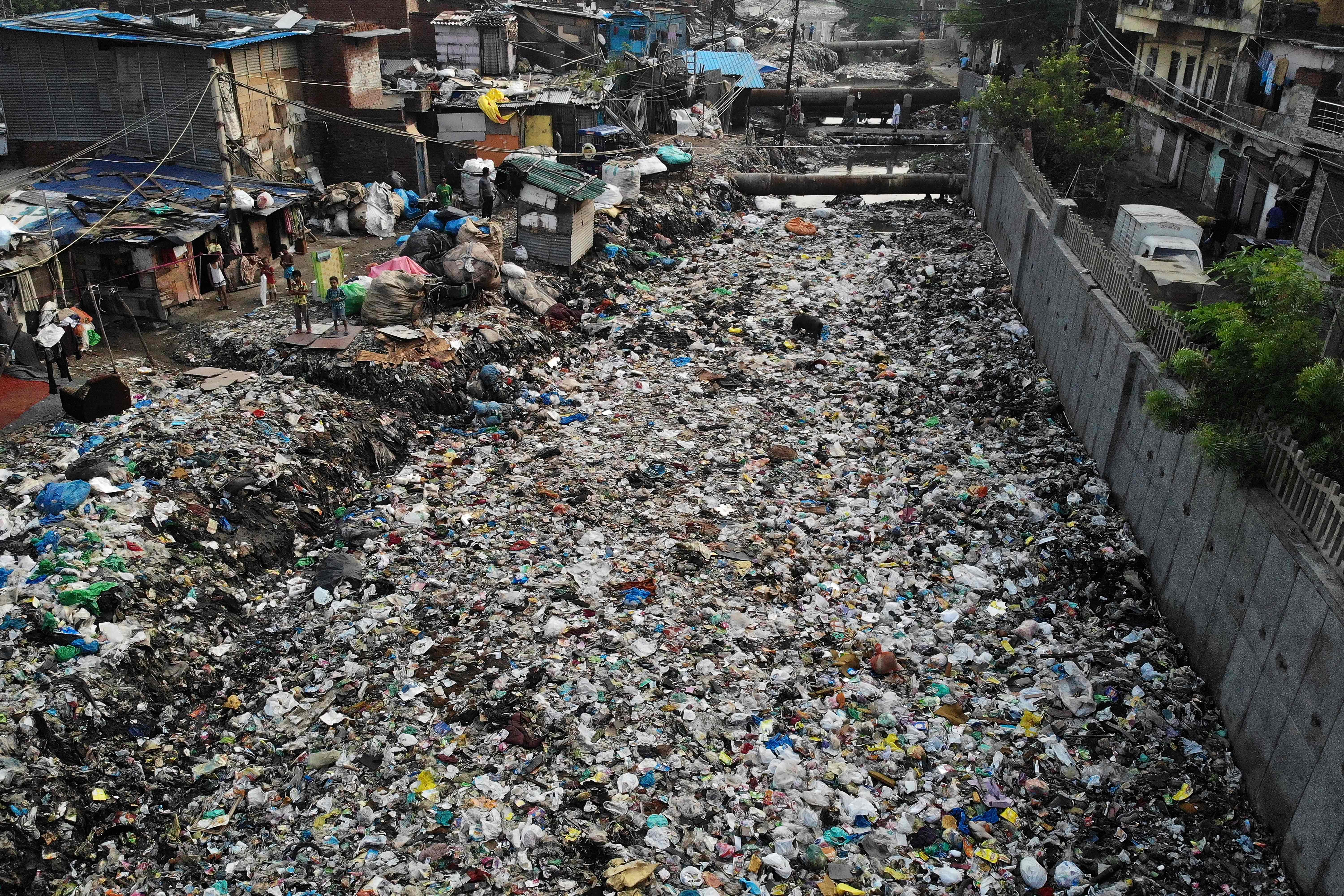 File: In this aerial photo taken on 4 October 2019, children (left) stand near a polluted sewage drain canal covered in garbage in a low-income neighborhood in New Delhi