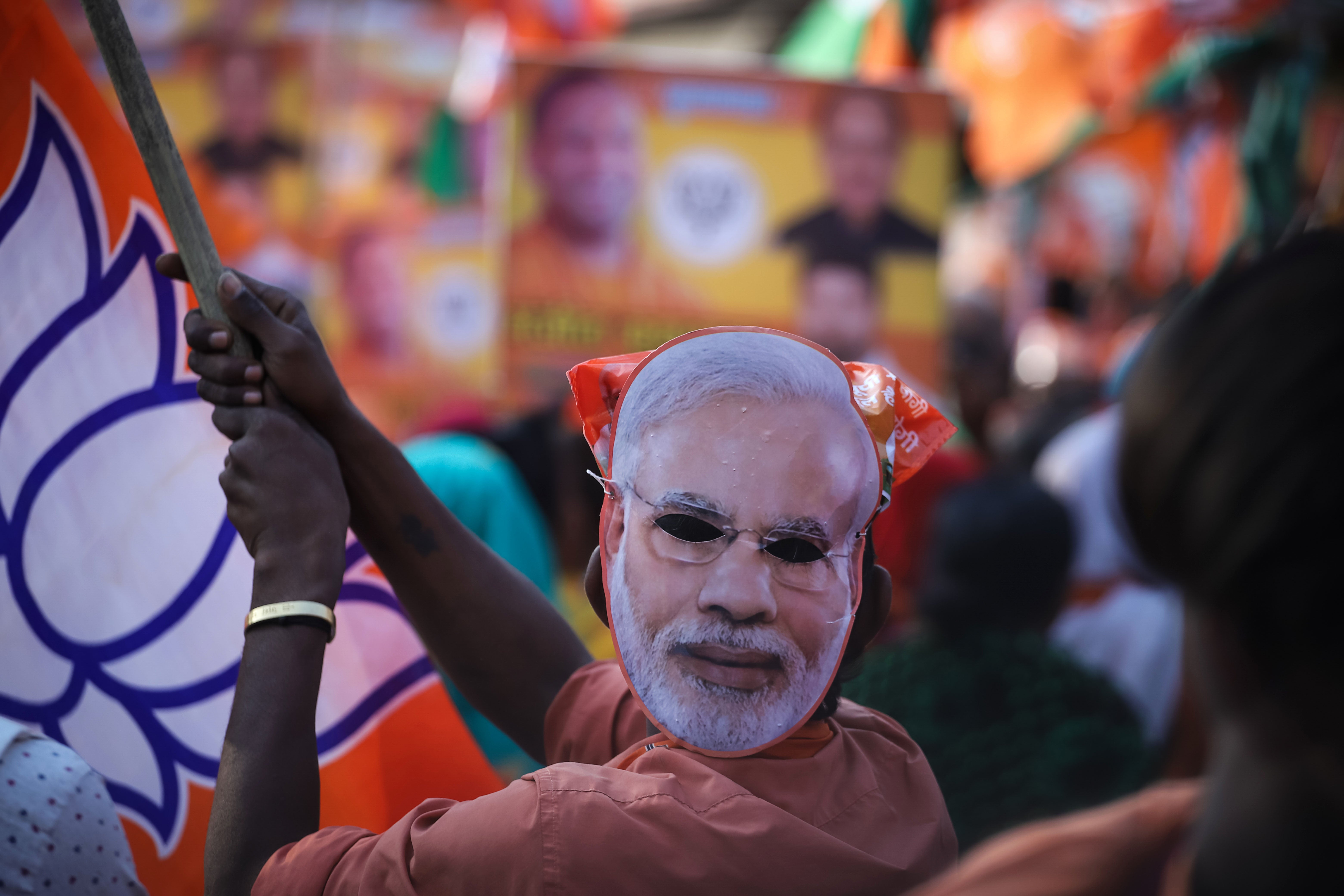 A BJP supporter wears a mask depicting Narendra Modi on the back of his head during a roadshow for Adityanath