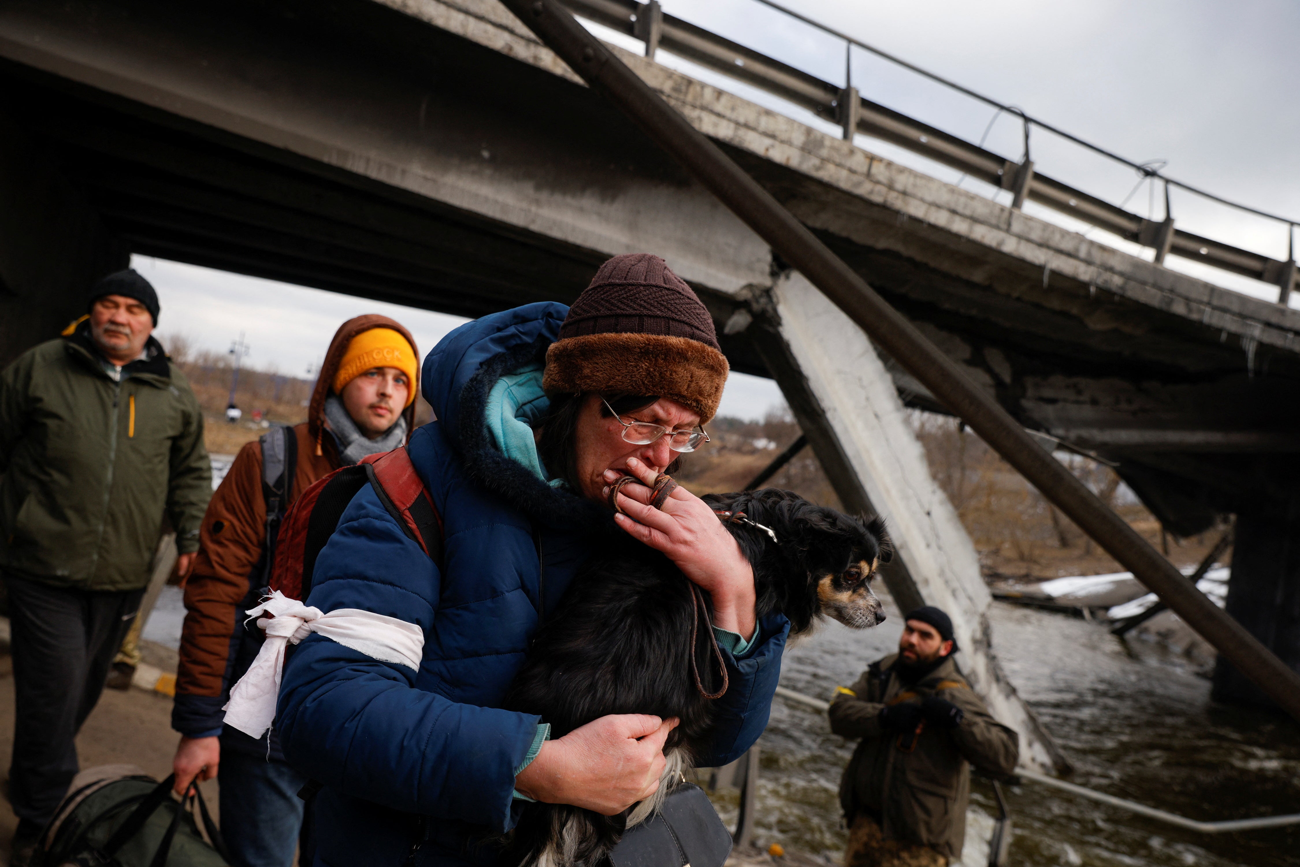 A man holds his dog as he walks below a destroyed bridge as Russia's attack on Ukraine continues in Irpin