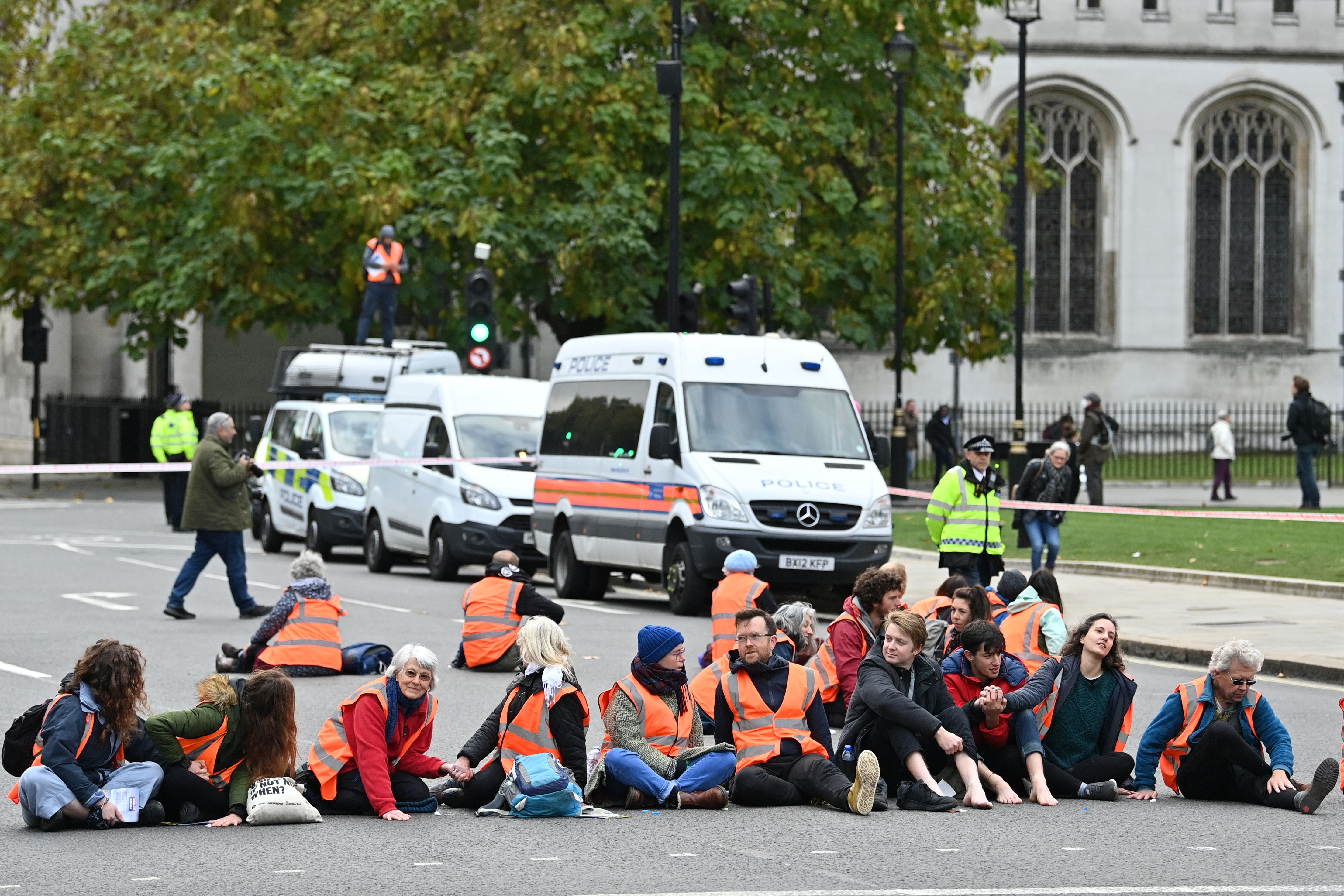 Police officers monitor environmental activists from the group Insulate Britain blocking a street at Parliament Square