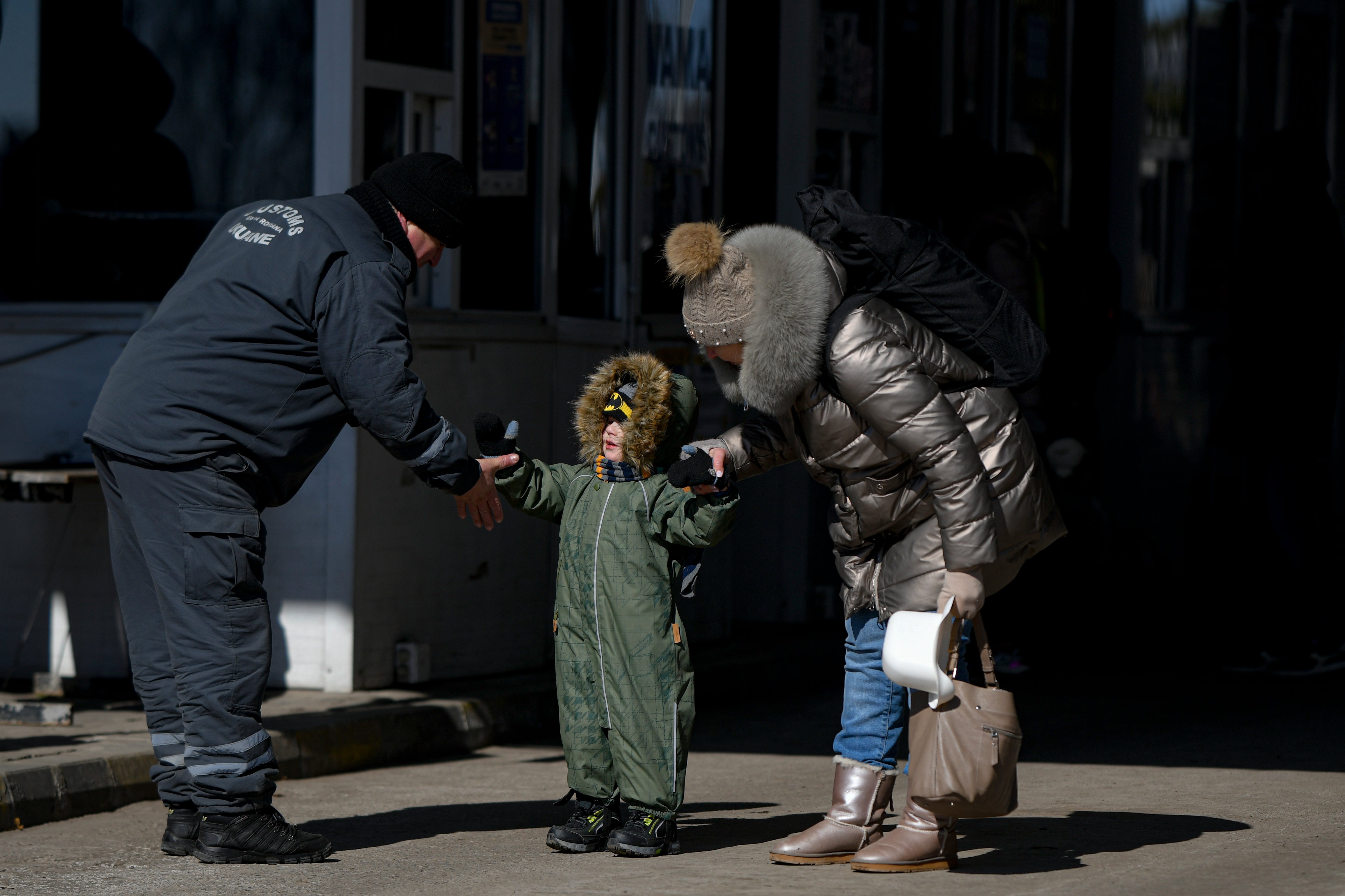 A customs employee holds his hand out to a refugee boy with his family at the Romanian-Ukrainian border, in Siret