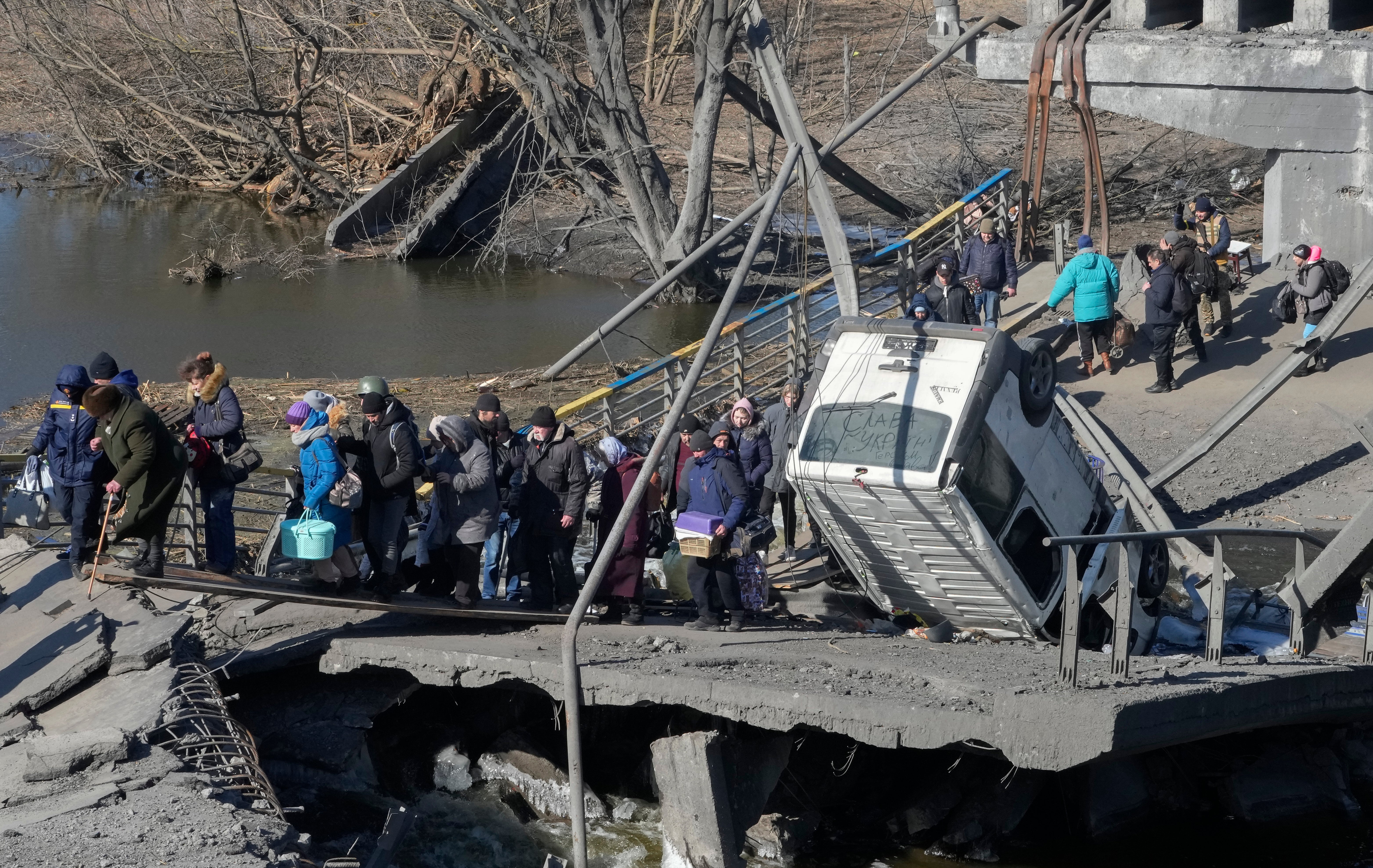 Ukrainians cross an improvised path under a destroyed bridge while fleeing Irpin