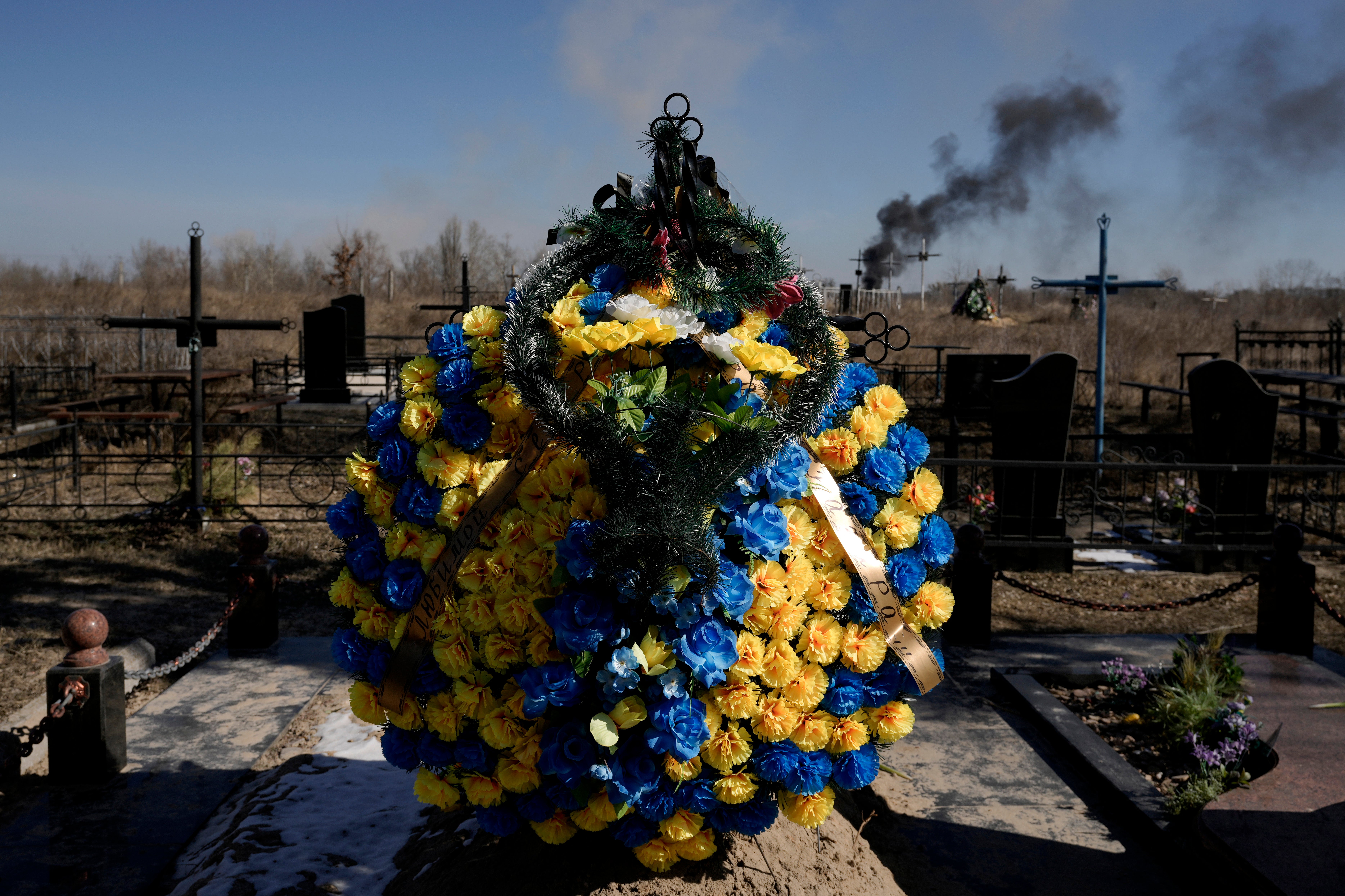 A smoke from shelling rises as a wreath of flowers is placed at a cemetery in Vasylkiv south west of Kyiv, Ukraine (Vadim Ghirda/AP)