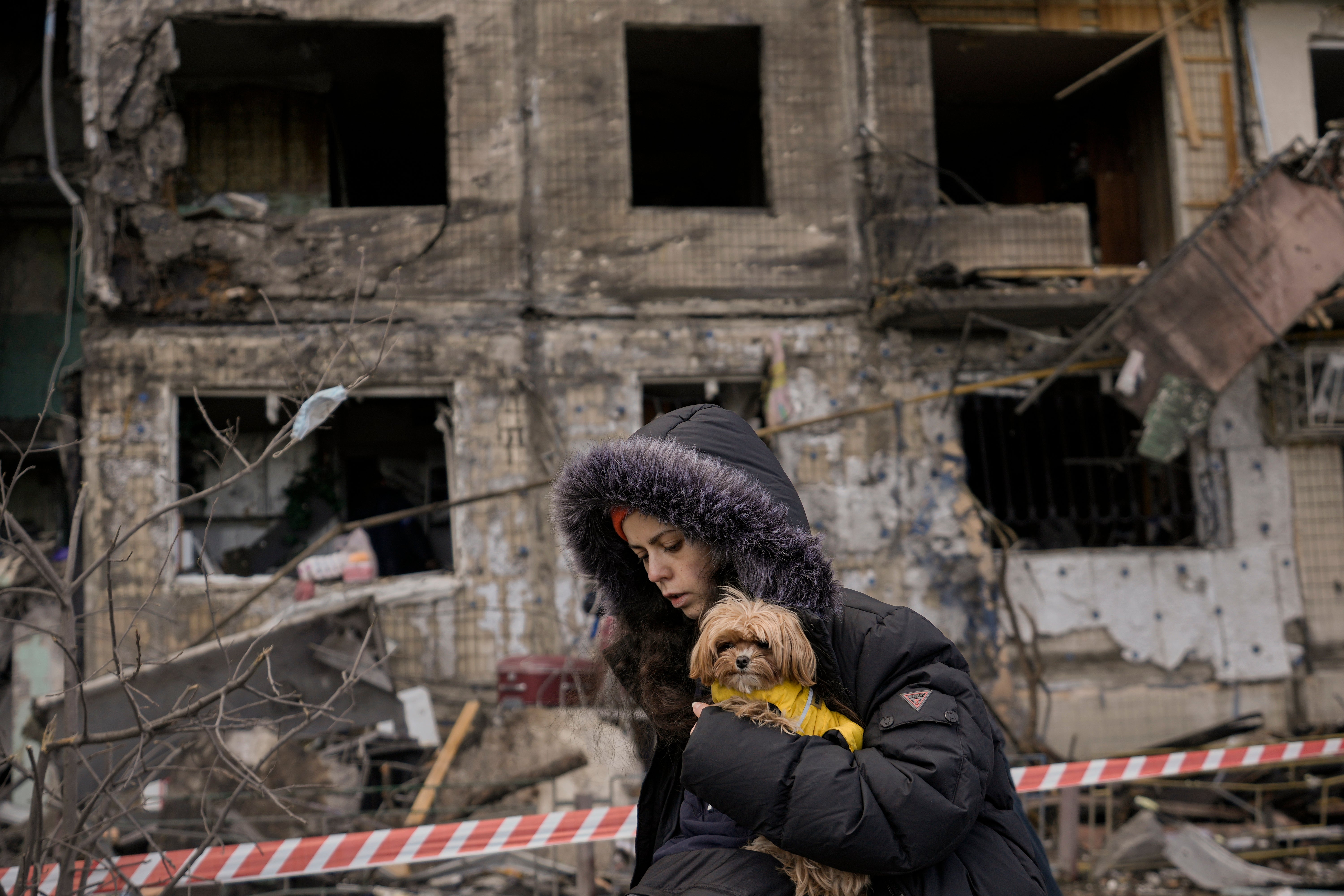 A woman holding a small dog walks in front of an apartment in a block which was destroyed by an artillery strike in Kyiv