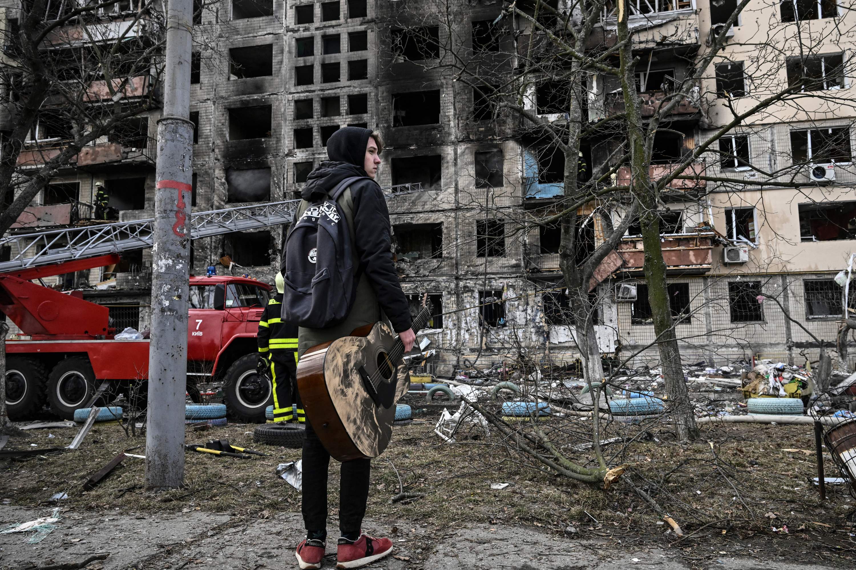 Maksim Korovii, 18, holds his guitar as he stands in front of his destroyed apartment building