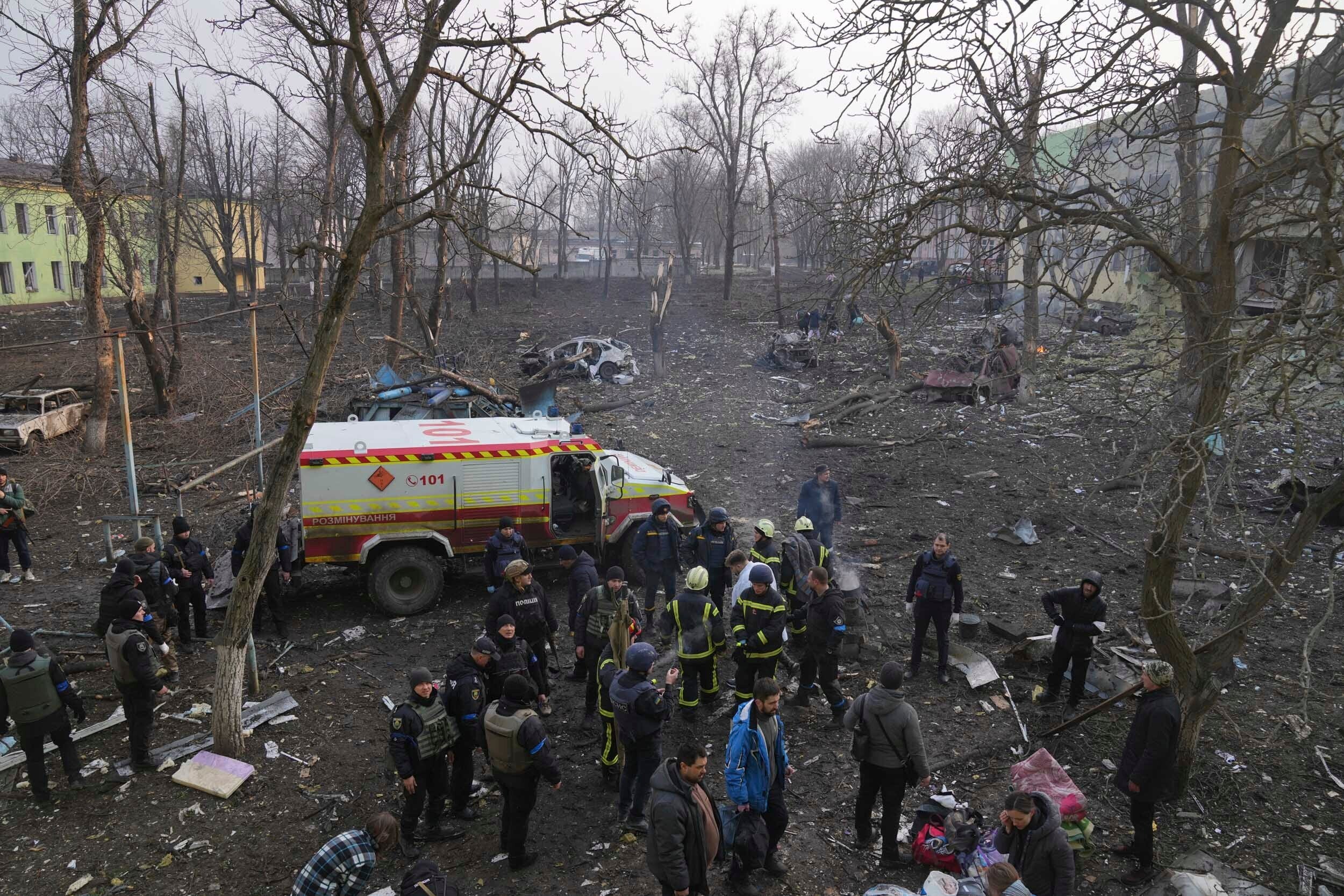 Ukrainian servicemen and firefighters stand in the area outside of a maternity hospital damaged in a shelling attack in Mariupol