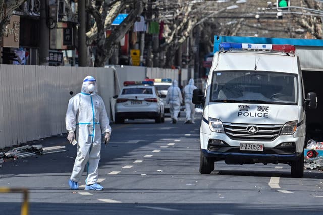 Un funcionario (L) se para en una calle mientras se usan barreras (atrás L) para cerrar un área después de la detección de nuevos casos de Covid-19 en Shanghái.