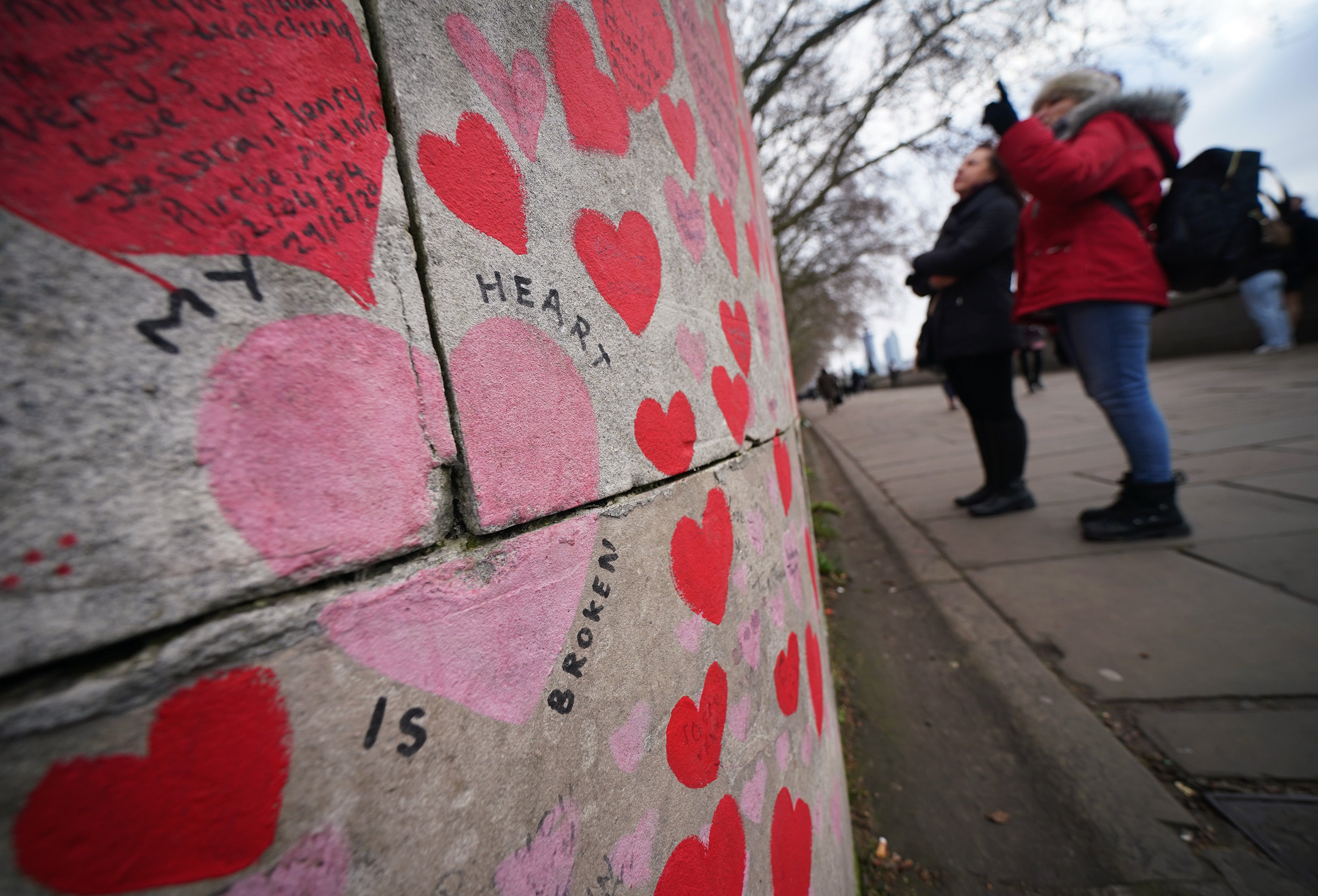 People stop to look at tributes on the Covid memorial wall in Westminster, central London (Yui Mok/PA)