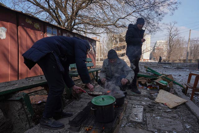 <p>Men cook a meal in a street in Mariupol</p>