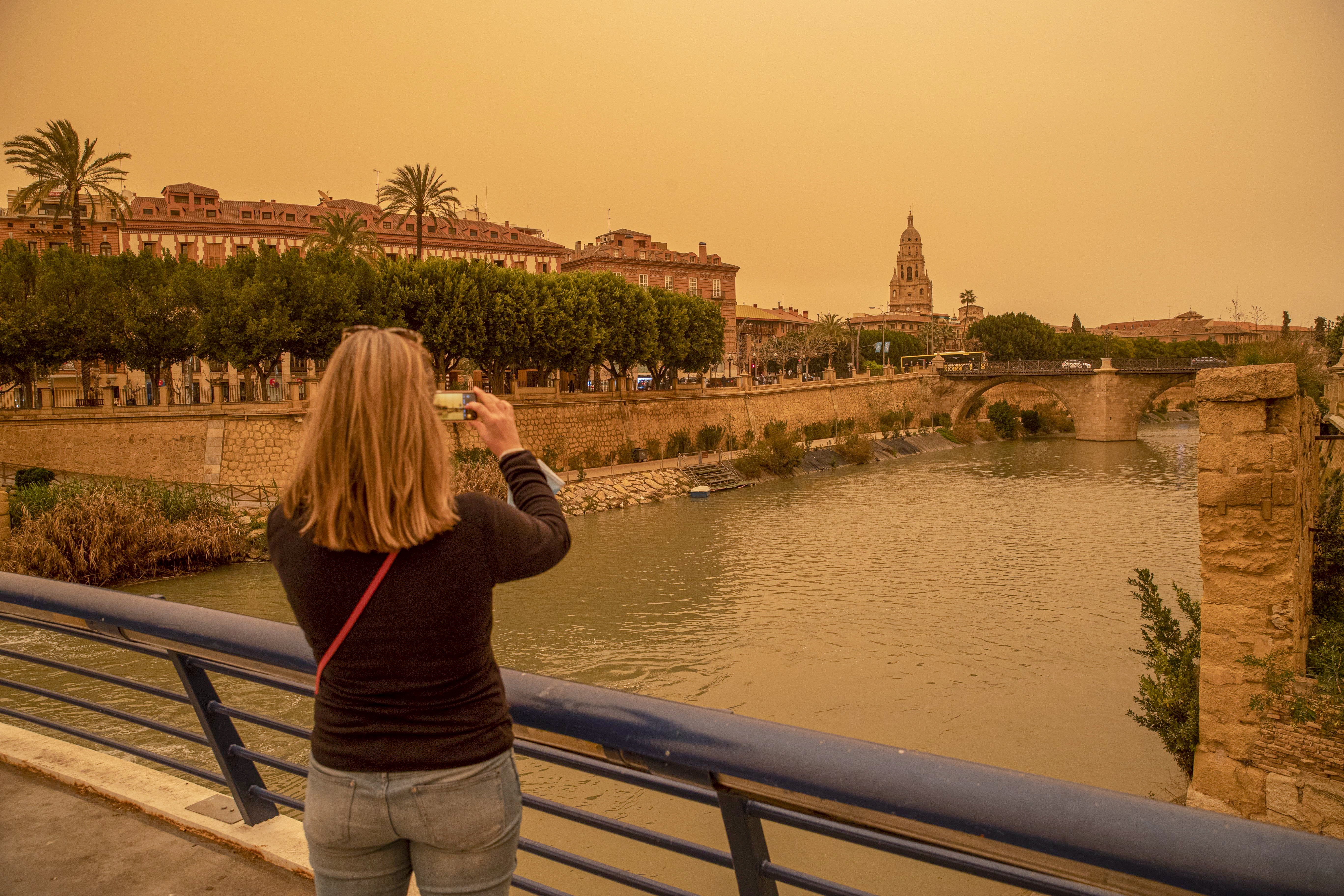 A woman takes a photo of the downtown of Murcia, Spain orange-blanketed with heavy dust this week