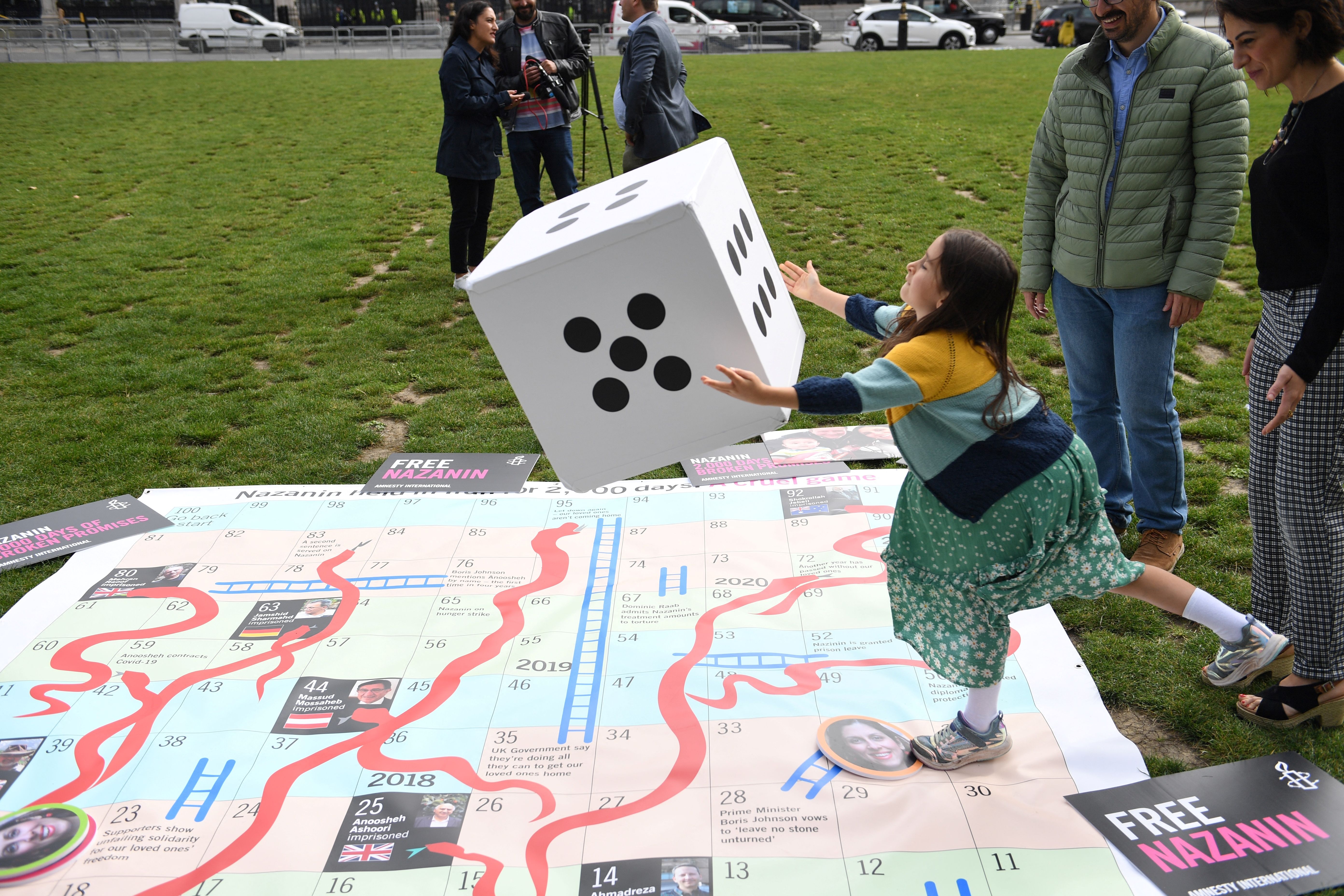 Gabriella Ratcliffe rolls a dice to play on a giant snakes and ladders board in Parliament Square, London to mark the 2,000th day of her mother’s detention in Iran