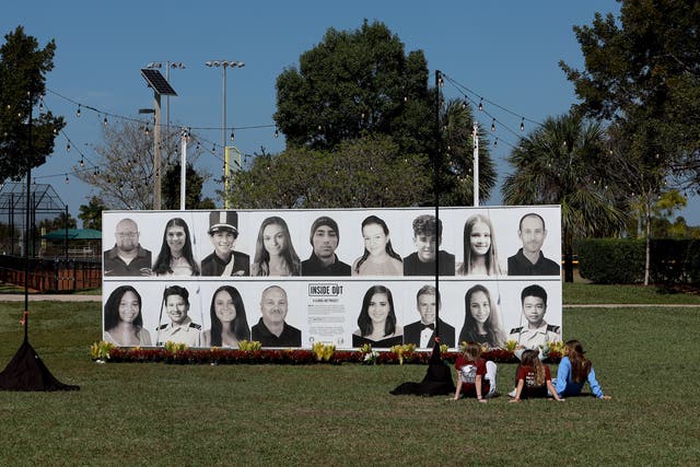 <p>People sit in front of a photo display of the 17 people killed at Marjory Stoneman Douglas High School during a mass shooting on February 14, 2022 in Pine Trails Park in Parkland, Florida</p>