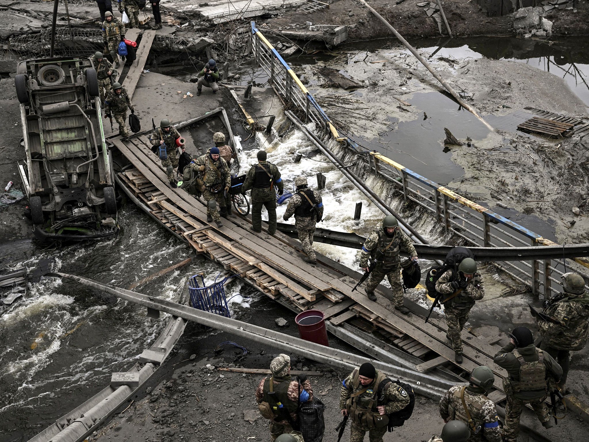 Ukrainian servicemen cross a river next to a destroyed bridge near the city of Irpin