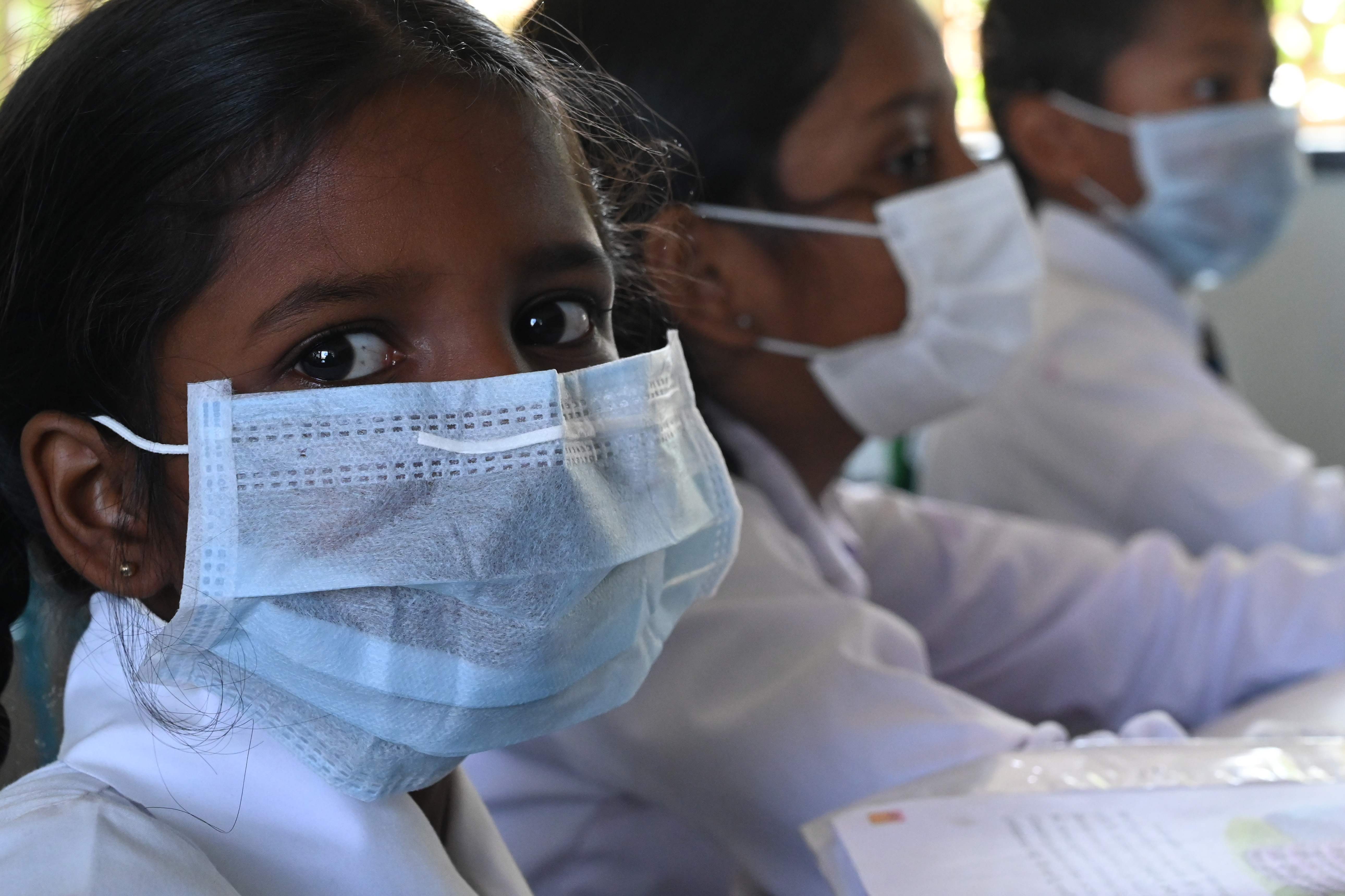 Sri Lanka’s schoolgirls look on as they sit in a classroom wearing facemasks