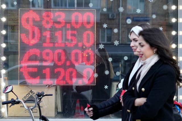 <p>People walk past a currency exchange office screen displaying the exchange rates of US dollar and euro to Russian rubles in Moscow</p>
