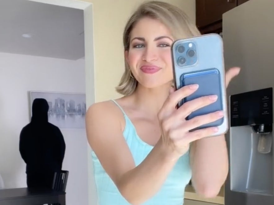 TikTok influencer Miranda Derrick in a video mocking her family’s concerns that she has been indoctrinated into a cult. The man looming in the background is her husband James, and is jokingly meant to portray a shadowy figure controlling Ms Derrick.