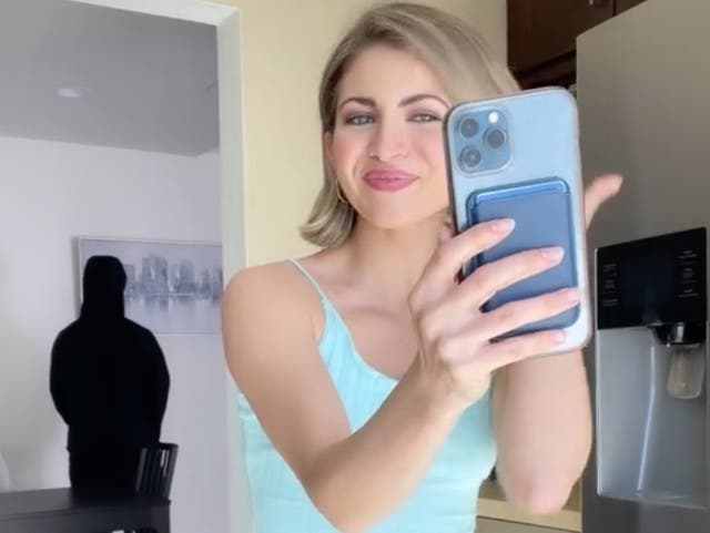 <p>TikTok influencer Miranda Derrick in a video mocking her family’s concerns that she has been indoctrinated into a cult. The man looming in the background is her husband James, and is jokingly meant to portray a shadowy figure controlling Ms Derrick.</p>