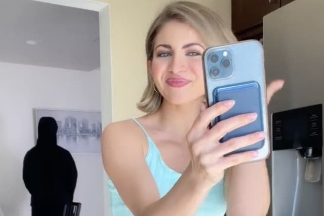 <p>TikTok influencer Miranda Derrick in a video mocking her family’s concerns that she has been indoctrinated into a cult. The man looming in the background is her husband James, and is jokingly meant to portray a shadowy figure controlling Ms Derrick.</p>