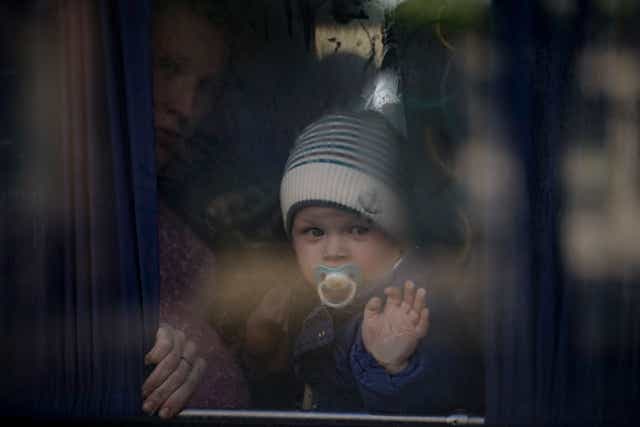 A refugee holds a baby while waiting on a bus for Ukrainian police to check papers and belongings in Brovary (Vadim Ghirda/AP)
