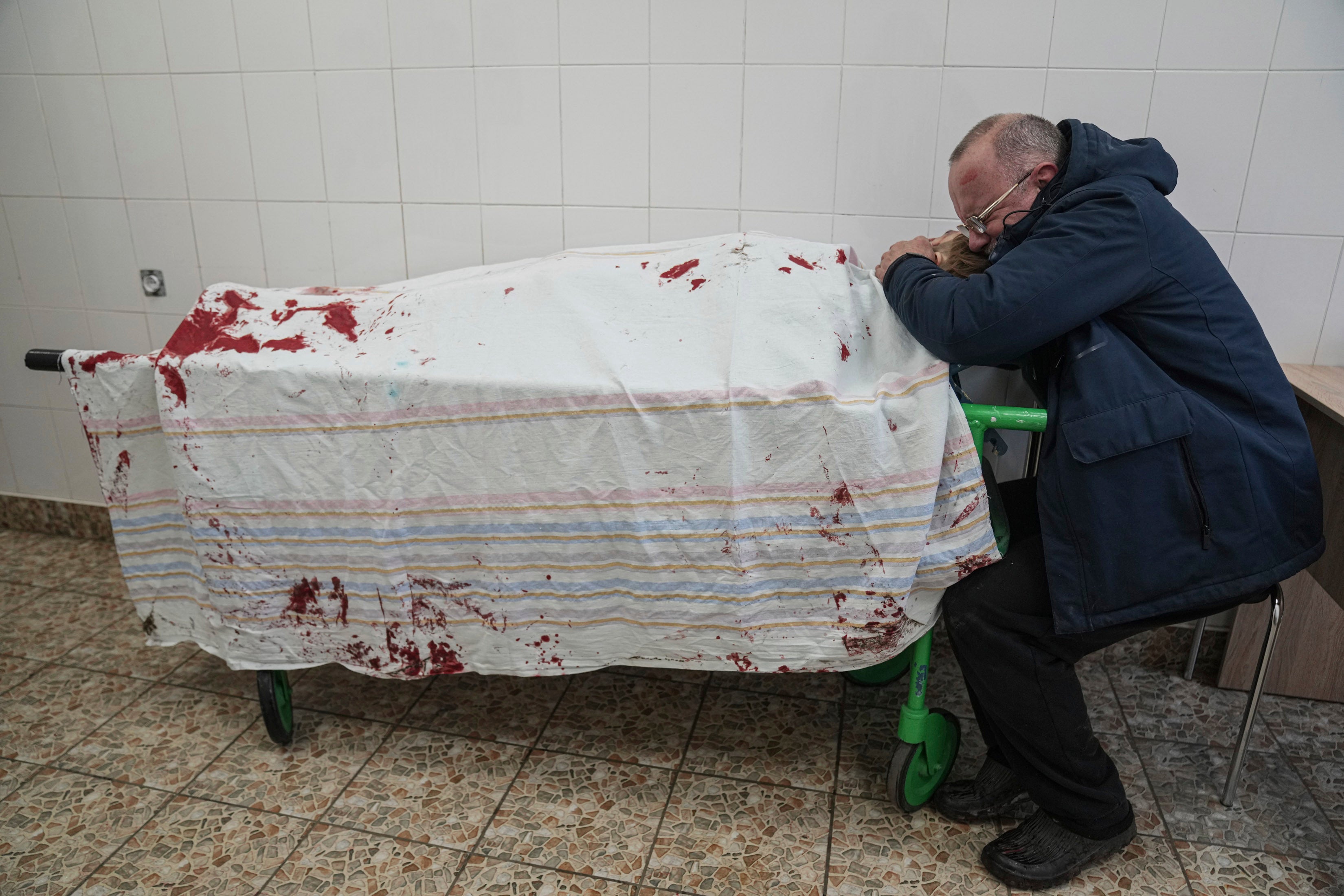 A father cries next to his teenage son’s lifeless body lying on a stretcher at a maternity hospital converted into a medical ward in Mariupol