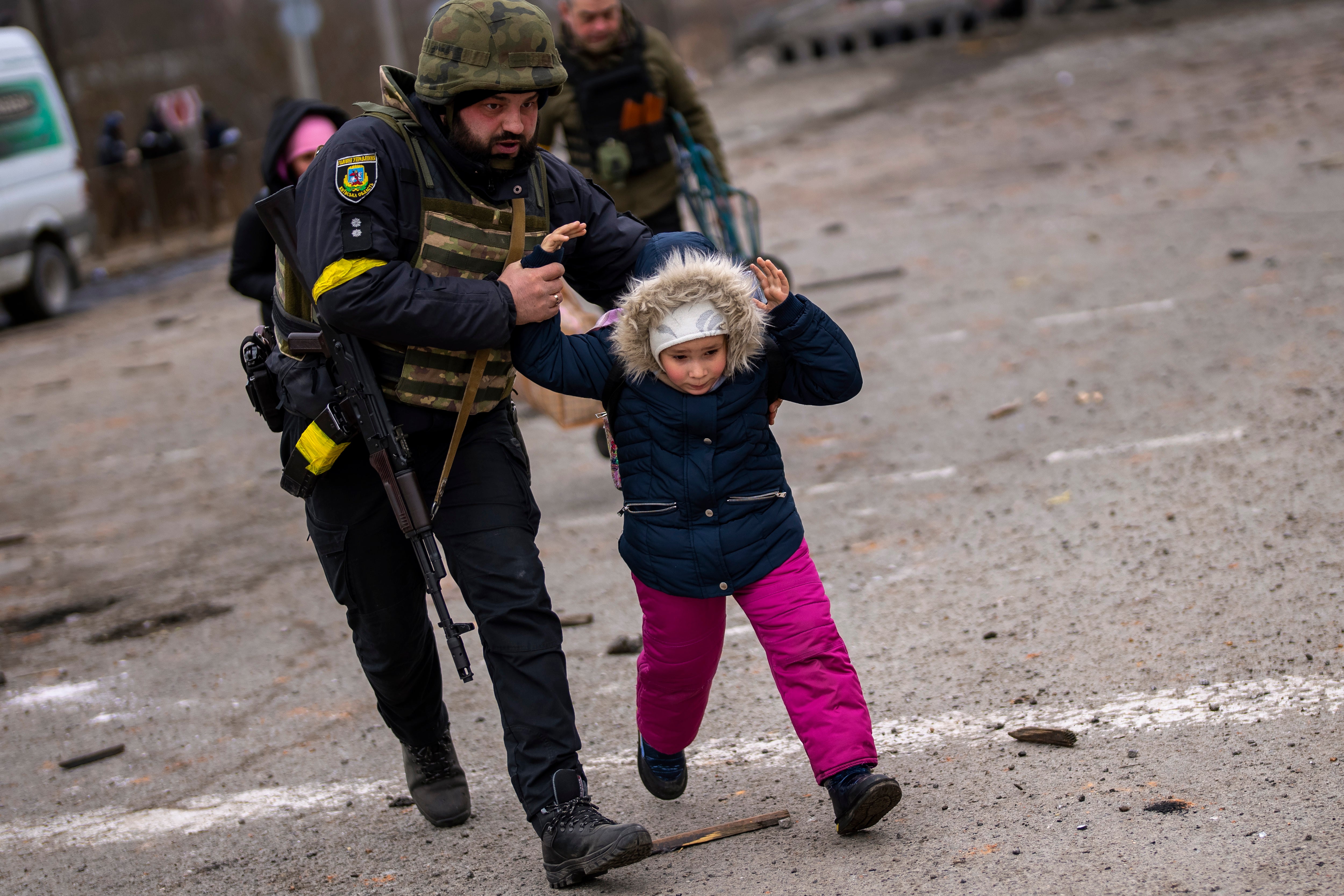 A Ukrainian police officer runs while holding a child as the artillery echoes nearby, while fleeing Irpin on the outskirts of Kyiv, Ukraine