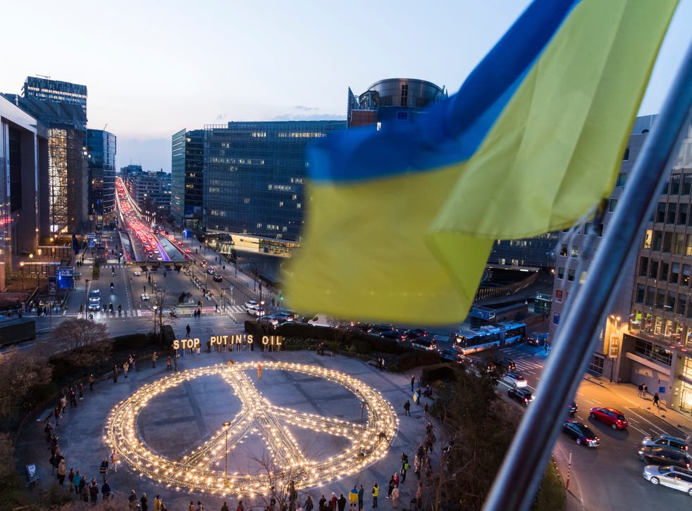 A Ukrainian flag flaps in the wind as a giant peace sign is put up by demonstrators ahead of an EU and Nato summit in Brussels (Geert Vanden Wijngaert/AP)