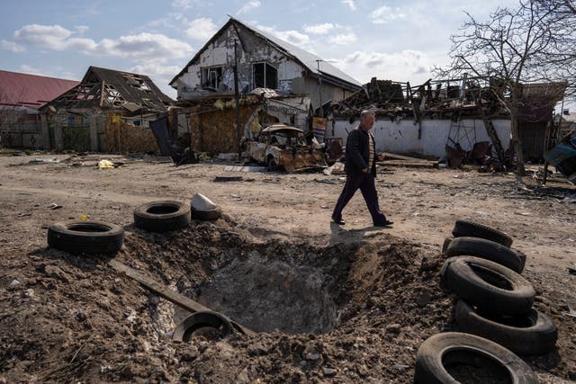 A man walks behind a crater created by a bomb and in front of damaged houses following a Russian bombing earlier this week, outskirts Mykolaiv, Ukraine (Petros Giannakouris/AP)