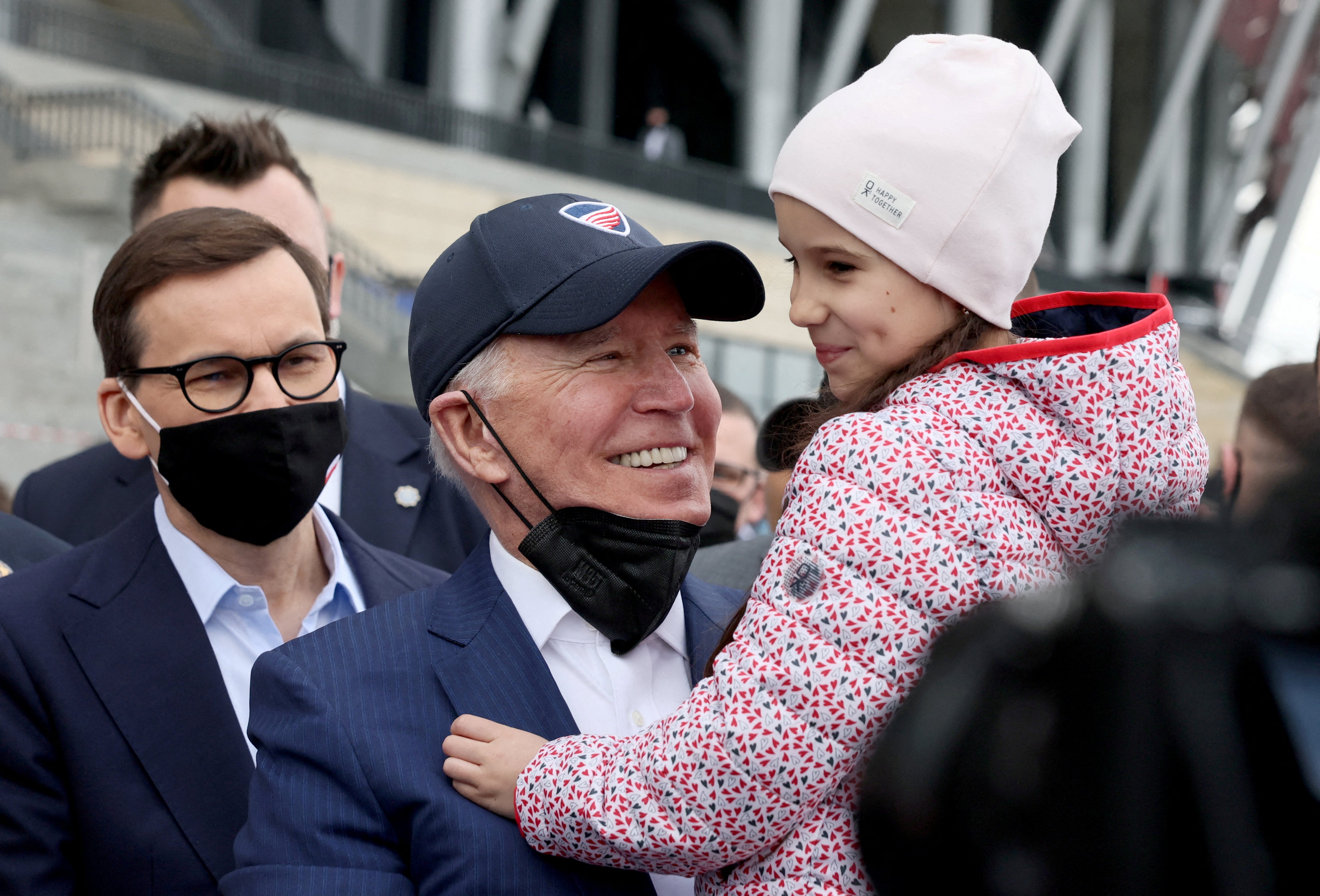 US president Joe Biden, flanked by Polish prime minister Mateusz Morawiecki, holds a child as he visits Ukrainian refugees at the PGE National Stadium in Warsaw, Poland