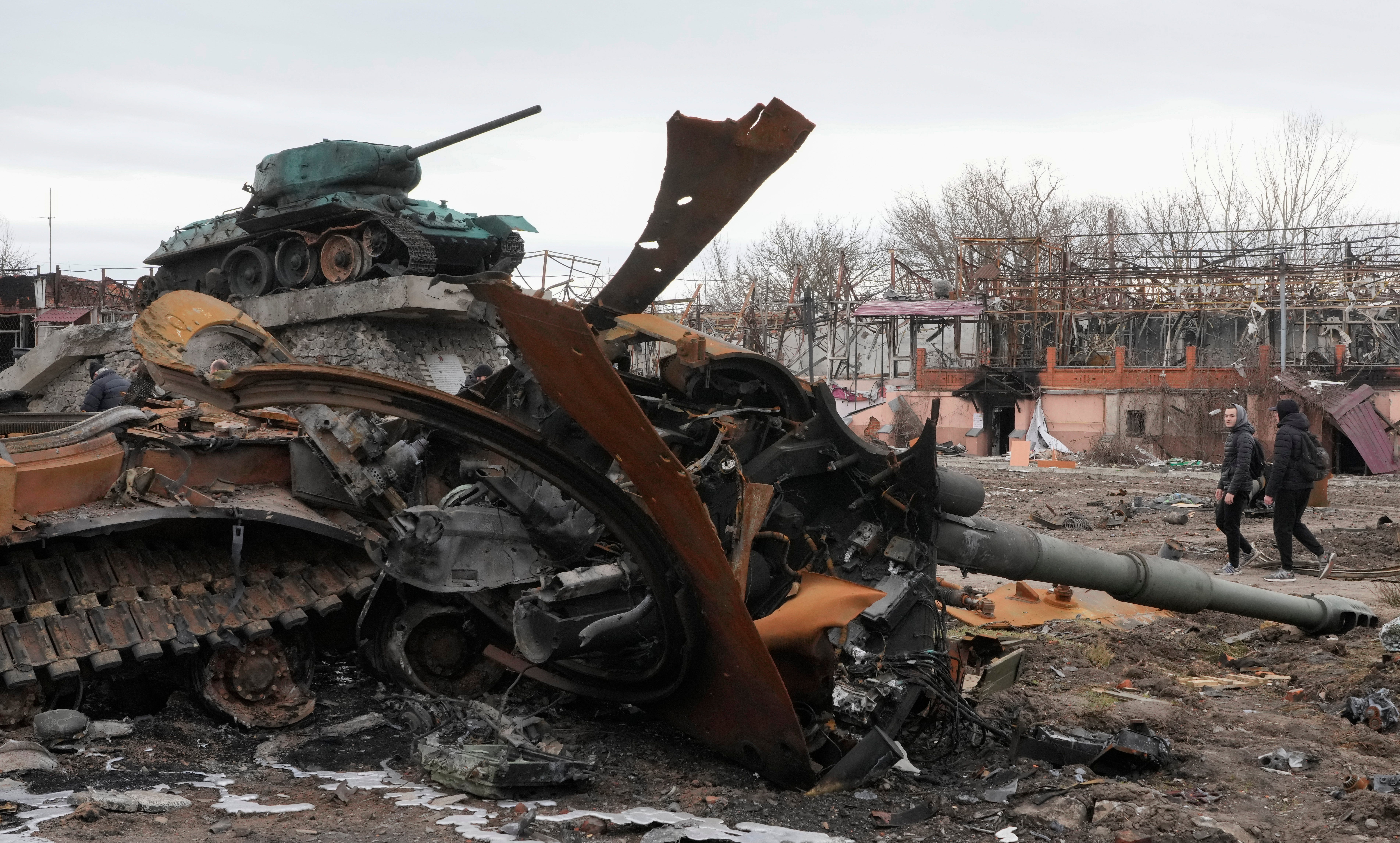 Local residents pass by a damaged Russian tank in a town east of Kyiv