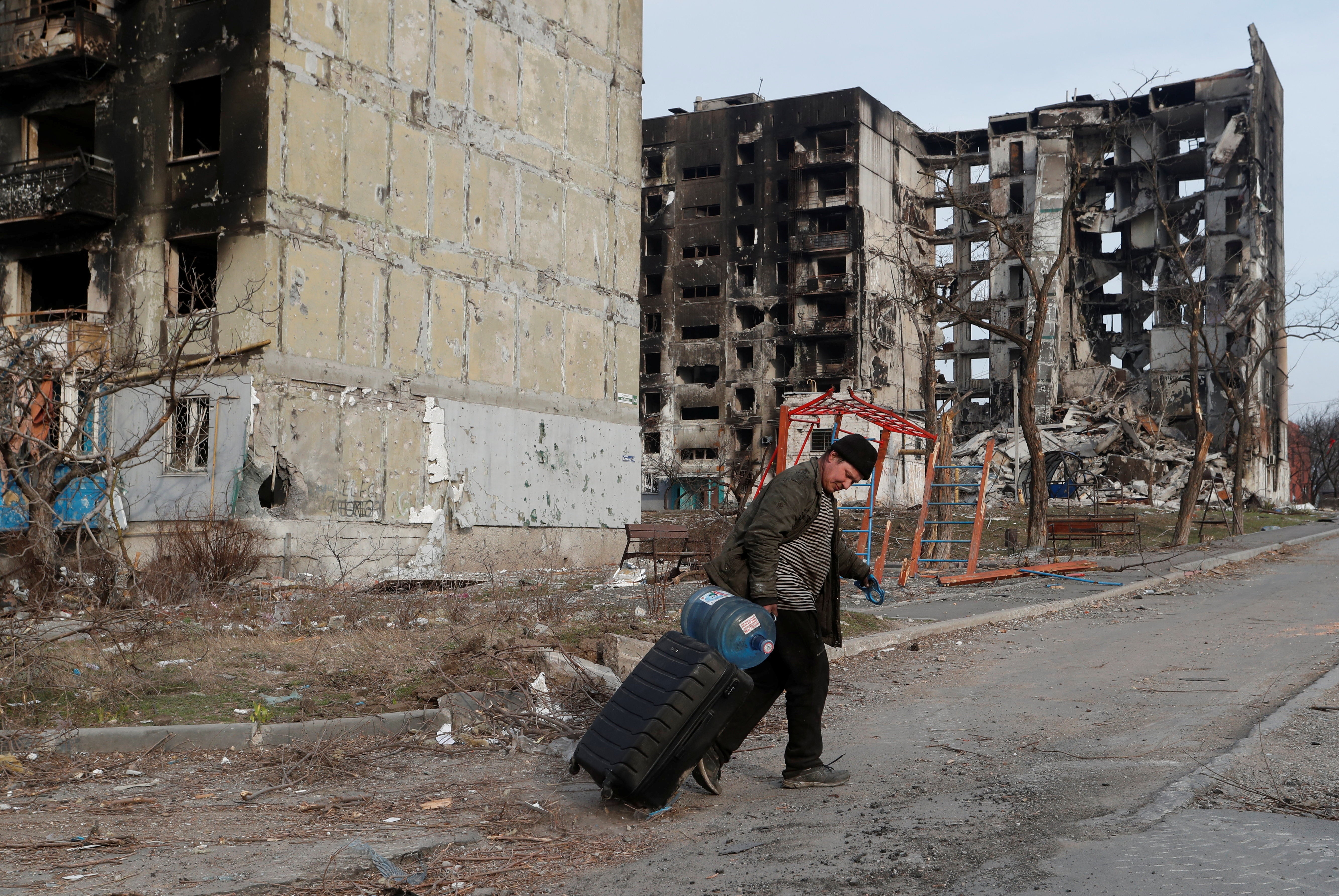 A local resident walks with a suitcase past apartment buildings destroyed during Ukraine-Russia conflict in the besieged southern port city of Mariupol